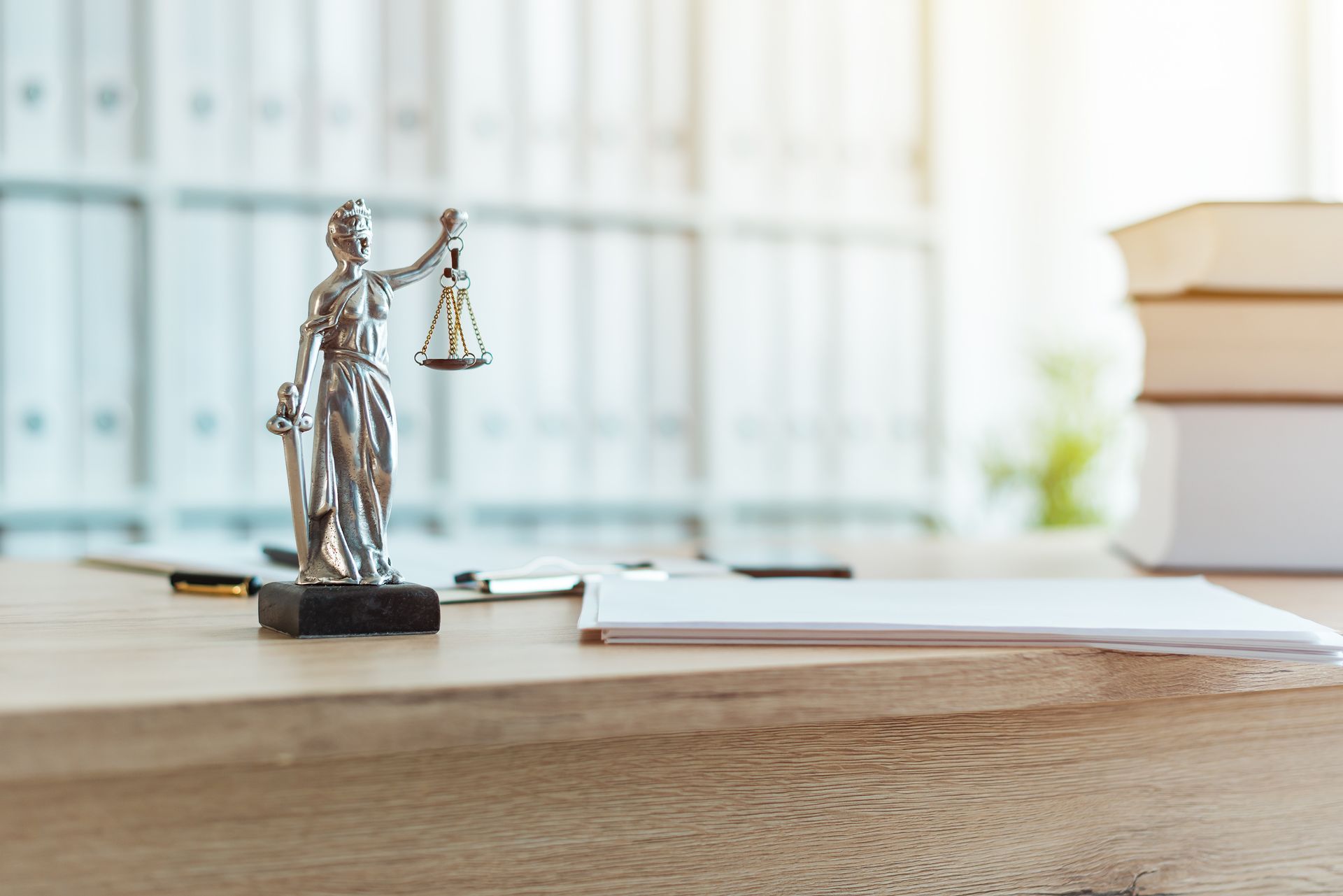 Statue of Lady Justice on a desk with paperwork and books, inside a bright office.