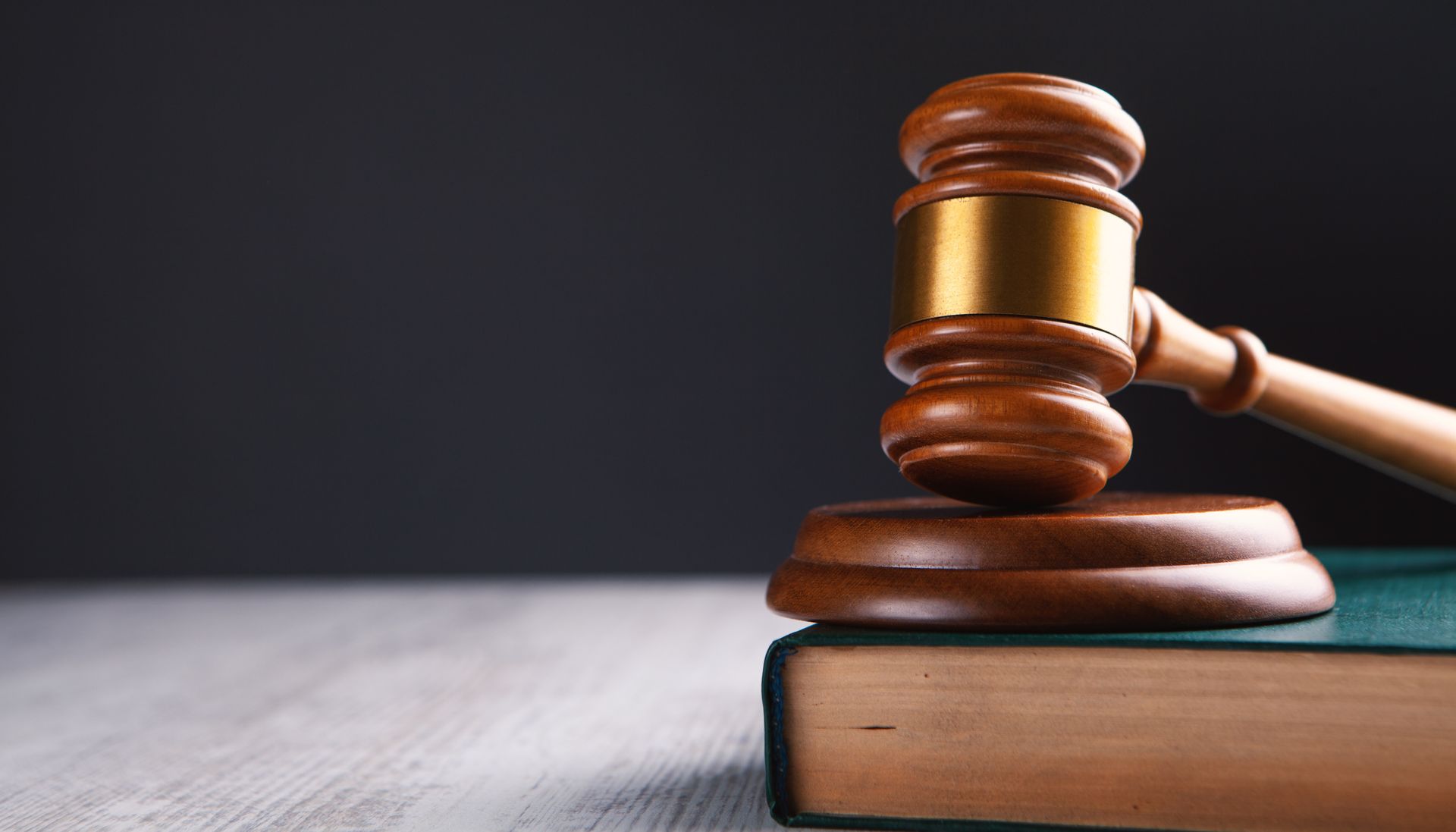 Wooden gavel on a stand atop a closed green book against a dark background.