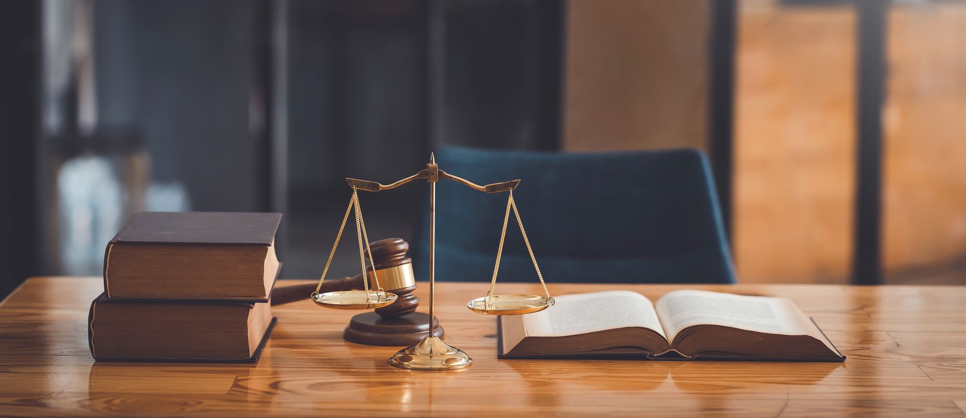 Books, scales, and gavel on a wooden desk. Law office setting with a blurred background.