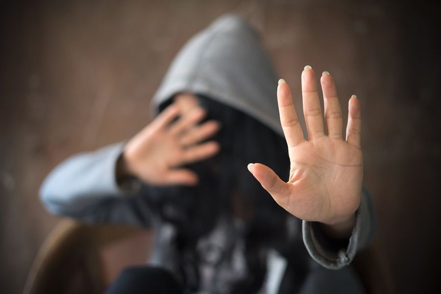 Person in gray hoodie, hands raised in front, blocking the face, indoors.
