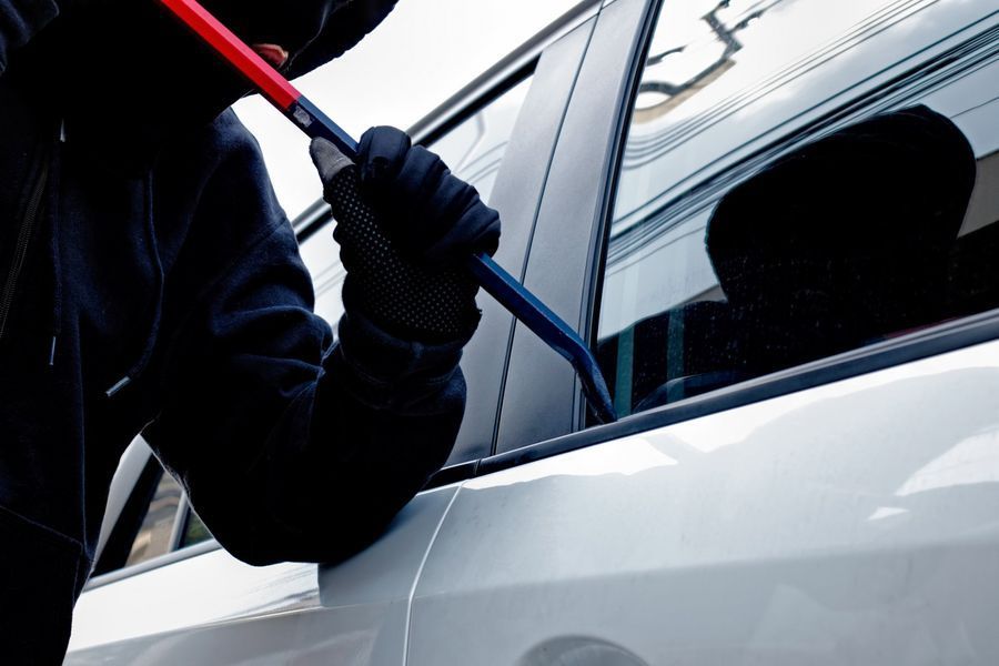 Person wearing dark clothing using a crowbar to pry open a car door window.
