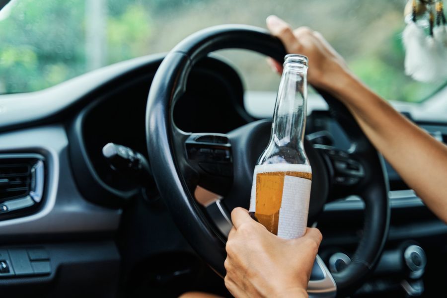 Person holding beer bottle while driving a car.