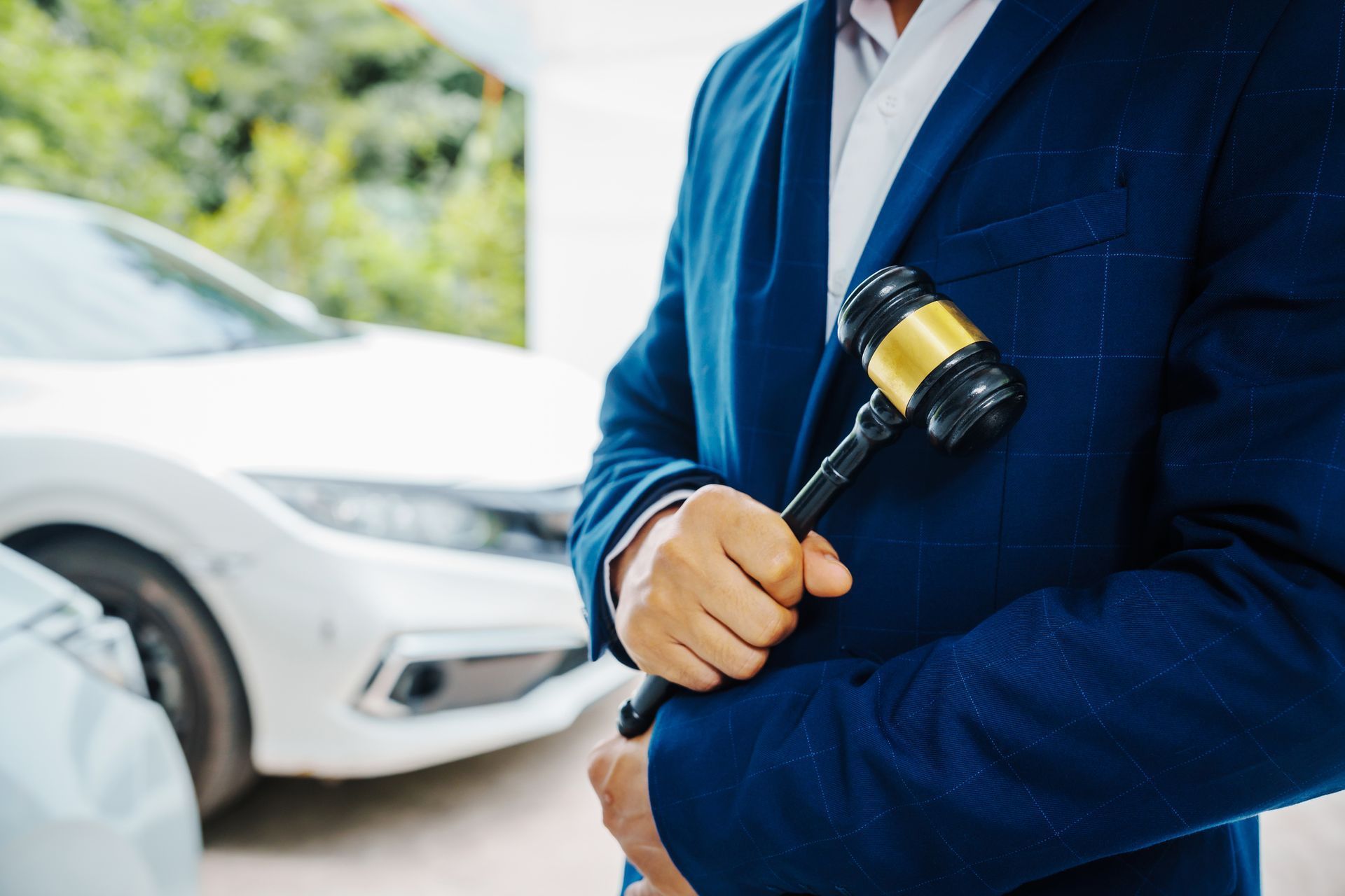 Man in blue suit holding a gavel near white car; possibly an auto auction.