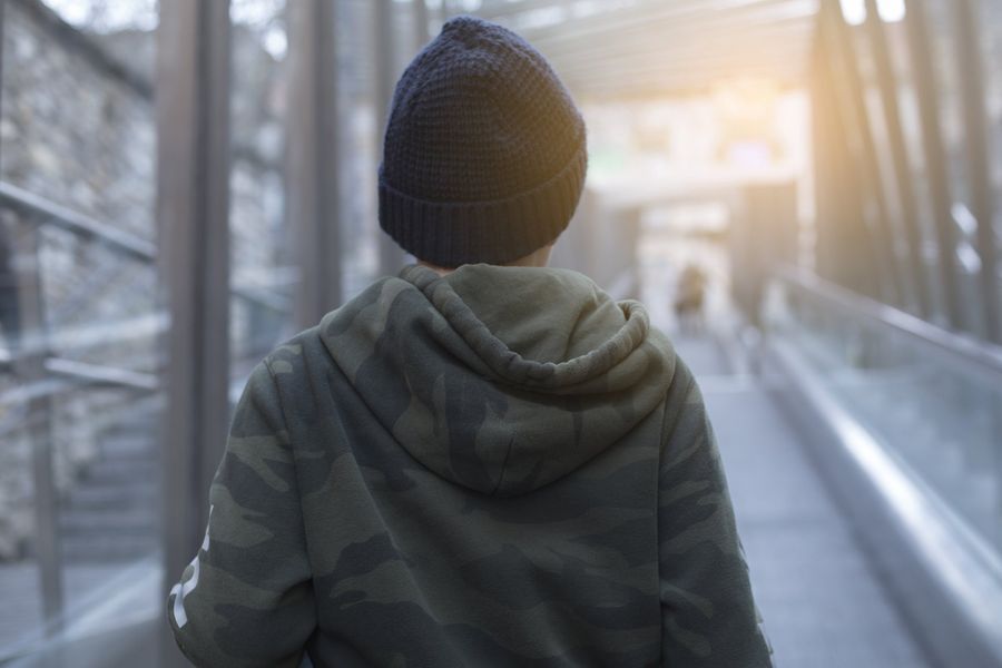 Person in a green hooded jacket and dark beanie walks down a moving walkway, lit by sunlight.