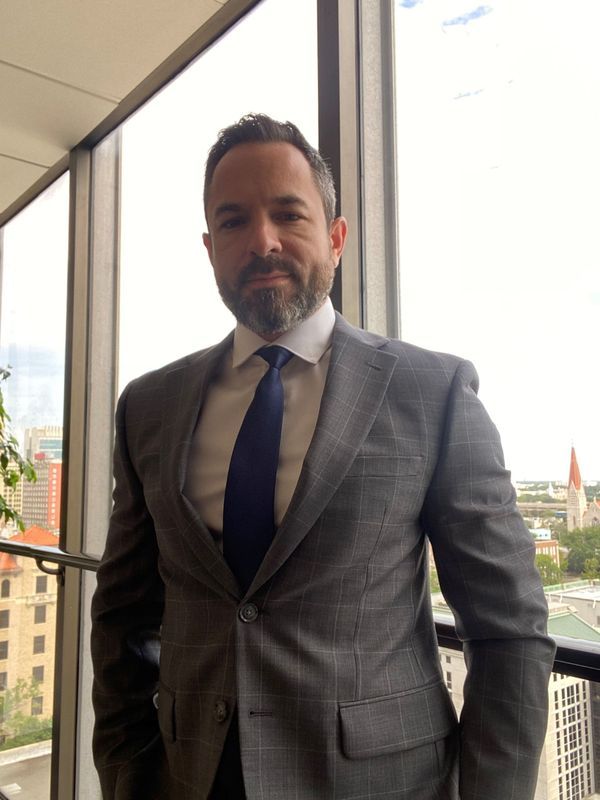 Man in a gray suit and navy tie stands near a window, overlooking a city.