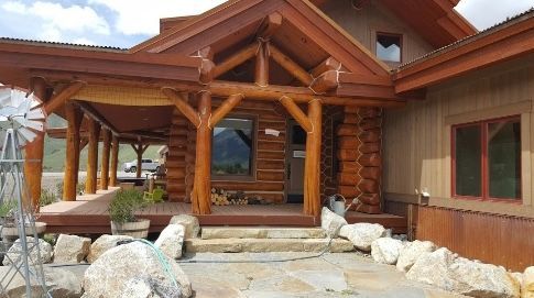 A large log cabin with a porch and a windmill in front of it.