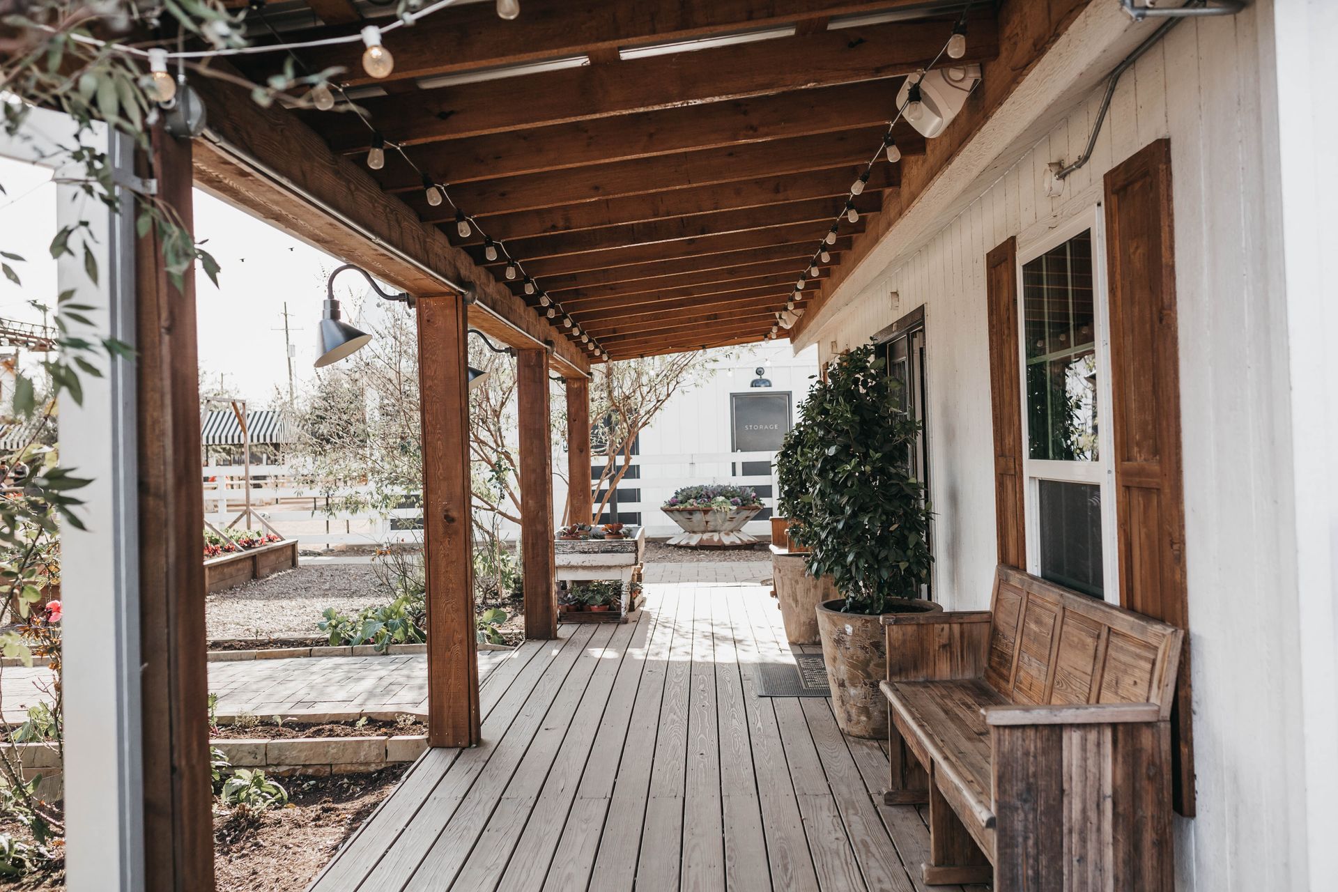 A wooden porch with a bench underneath it and a white building in the background.