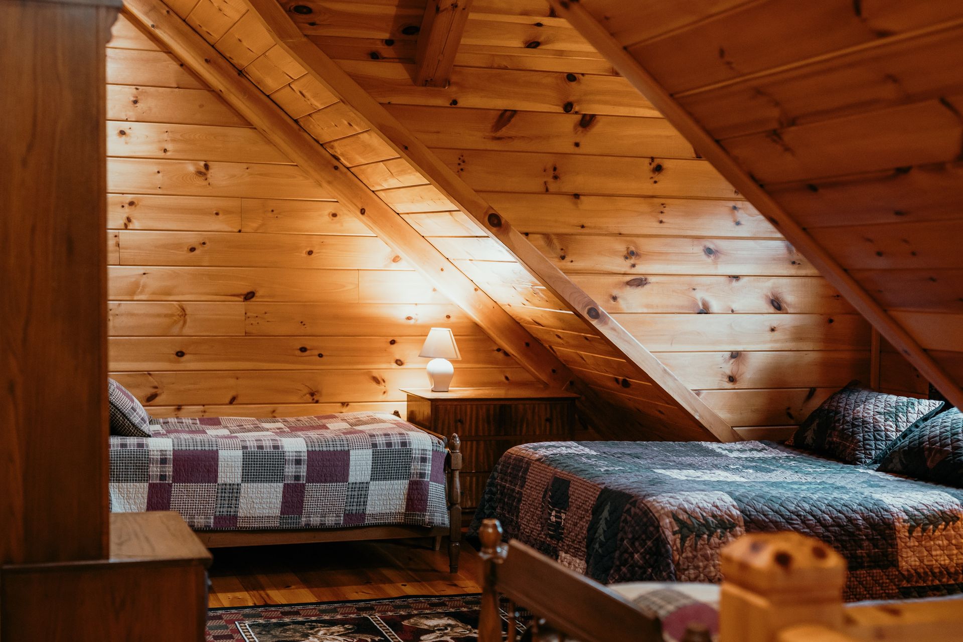 There are two beds in the attic of a wooden cabin.
