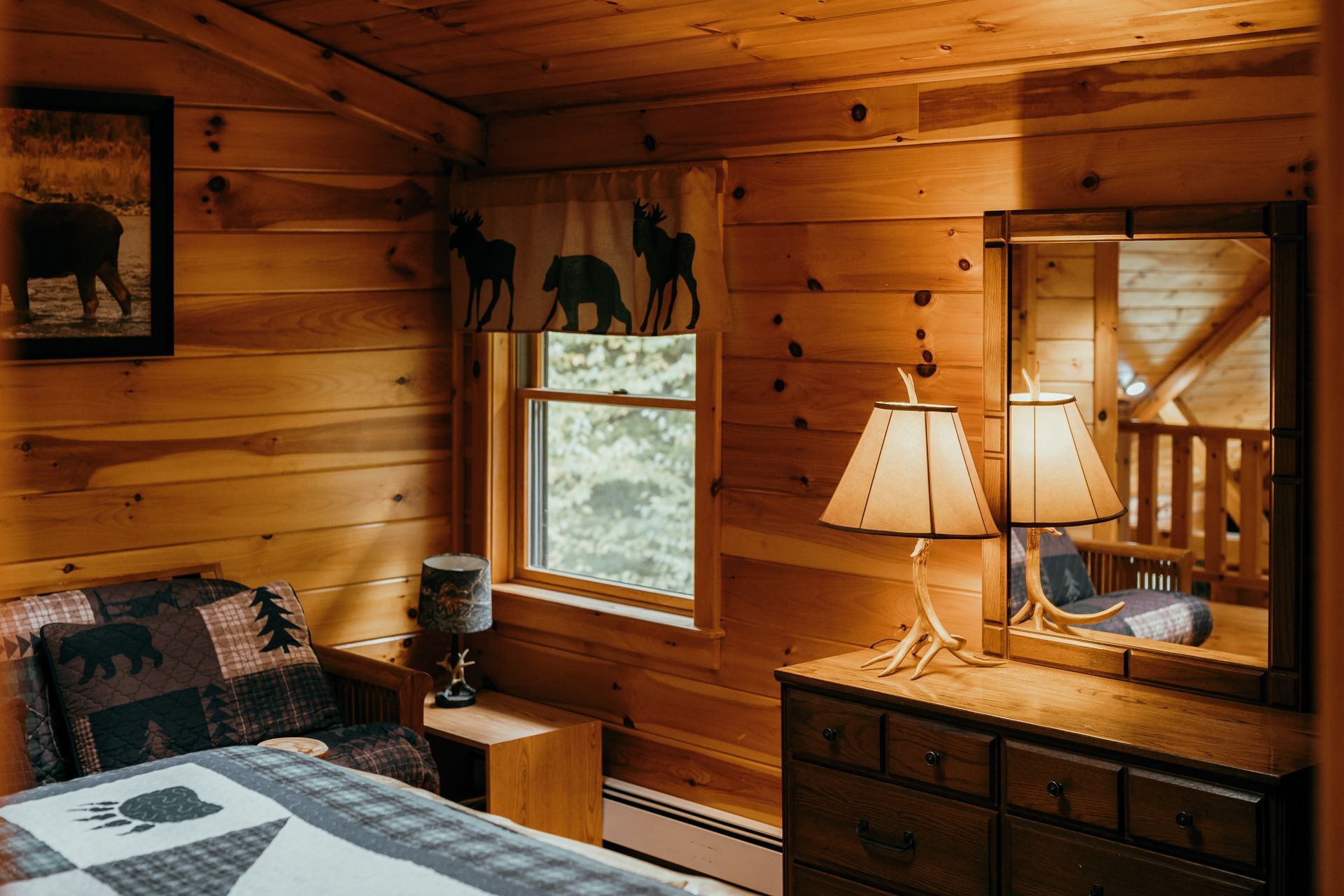 A bedroom in a log cabin with a bed , dresser , lamp and mirror.
