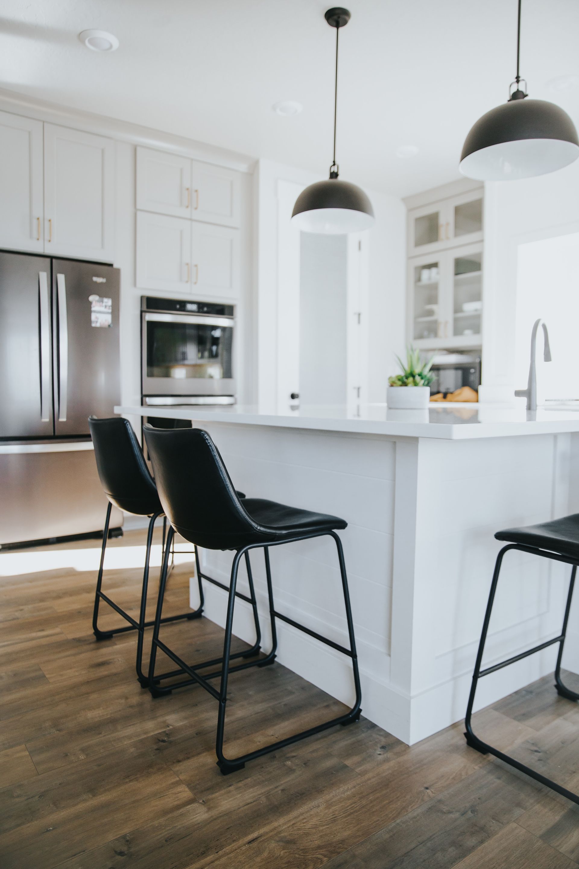 A kitchen with white cabinets , black chairs , a refrigerator , and a sink.
