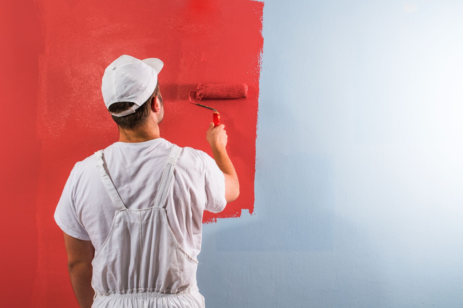 A man is painting a wall red with a paint roller.