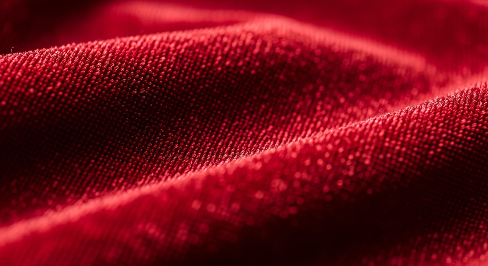 Close-up of vibrant red velvet fabric with soft folds and textured surface.
