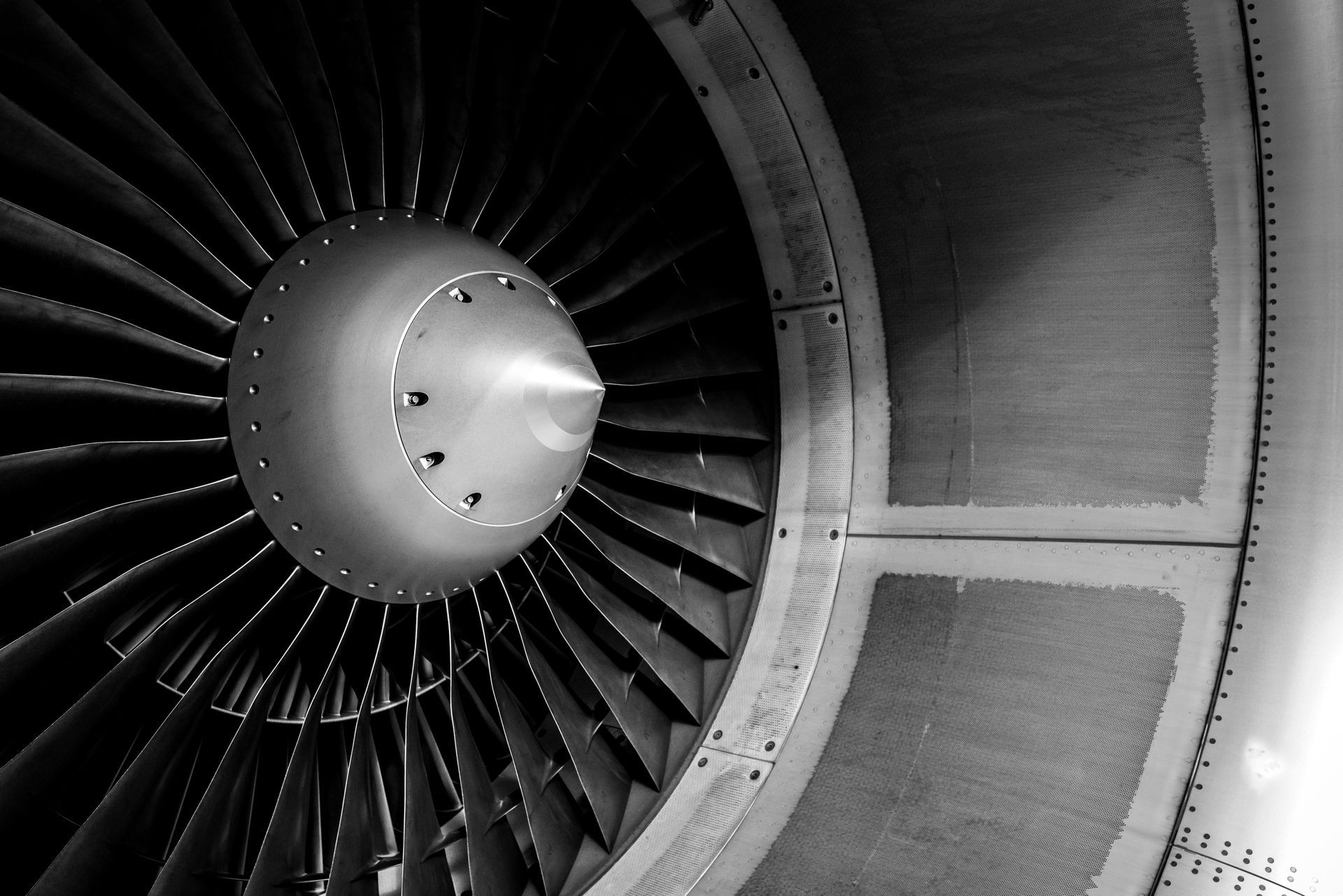 Black and white close-up of a jet engine, showing blades, central cone, and surrounding cowling.