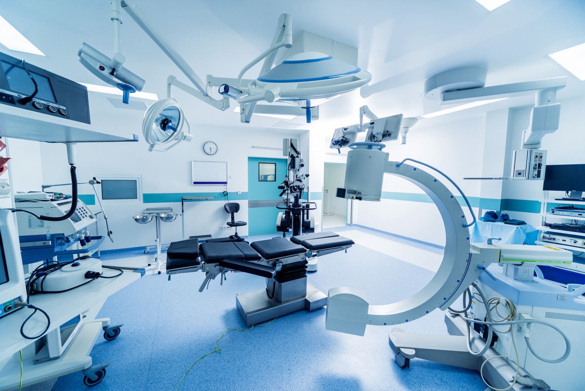 Modern operating room with surgical equipment and C-arm X-ray machine. Blue and white interior.
