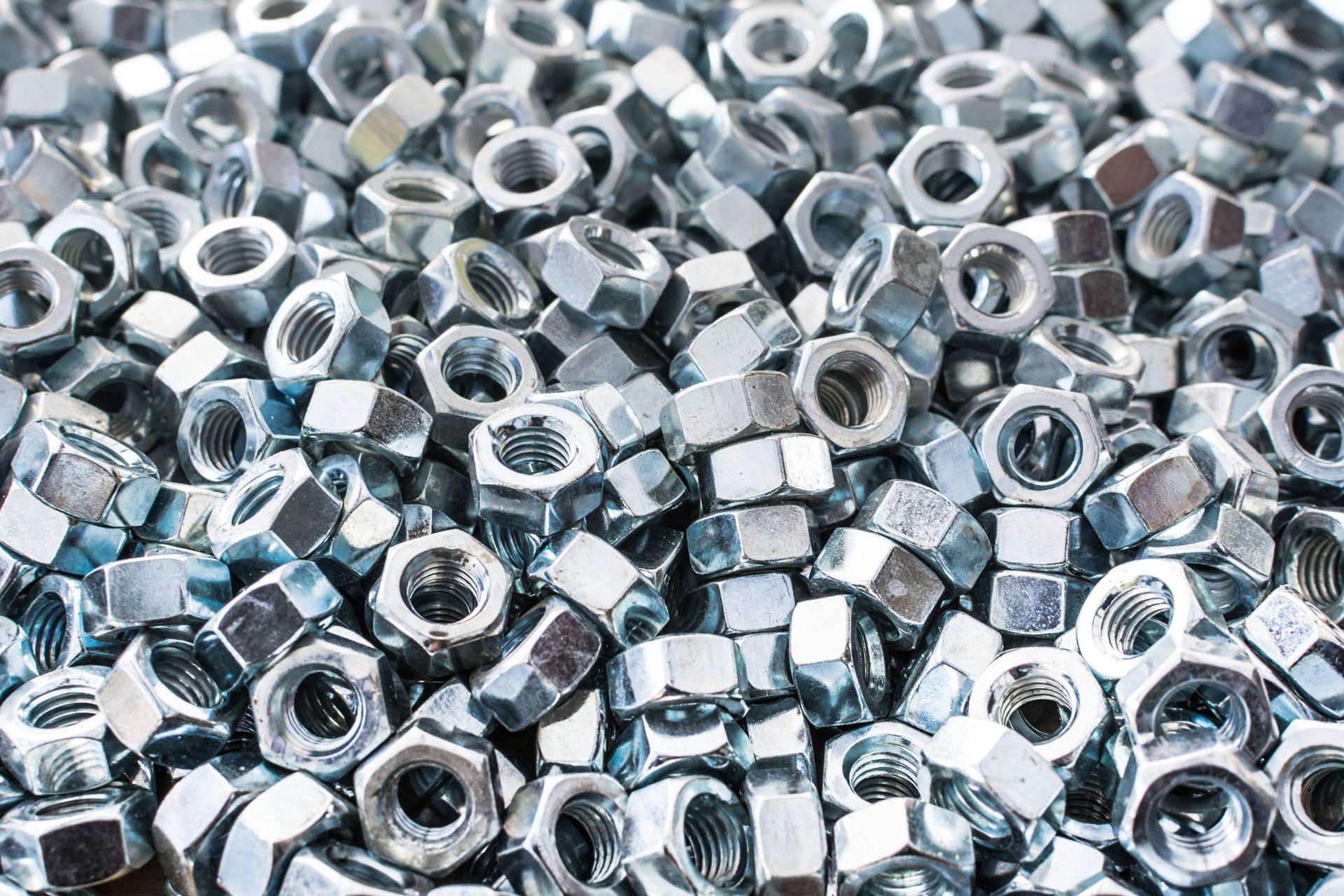 Pile of shiny, silver hex nuts.