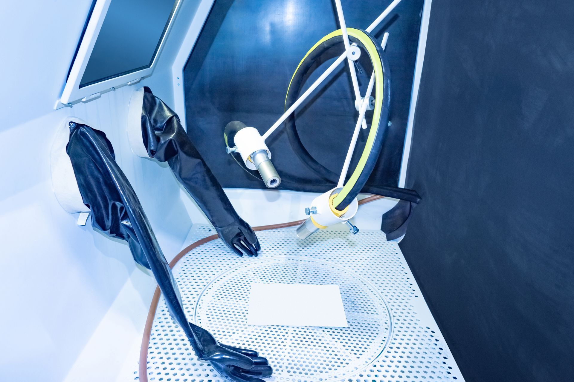 Inside a sandblasting cabinet: black gloves, a nozzle, and a clear plastic tray.