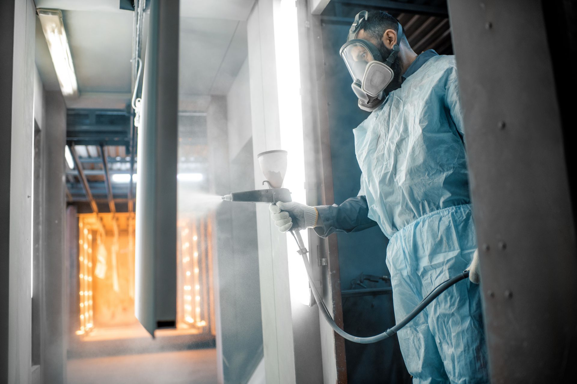 Person in protective suit spraying paint in a workshop.