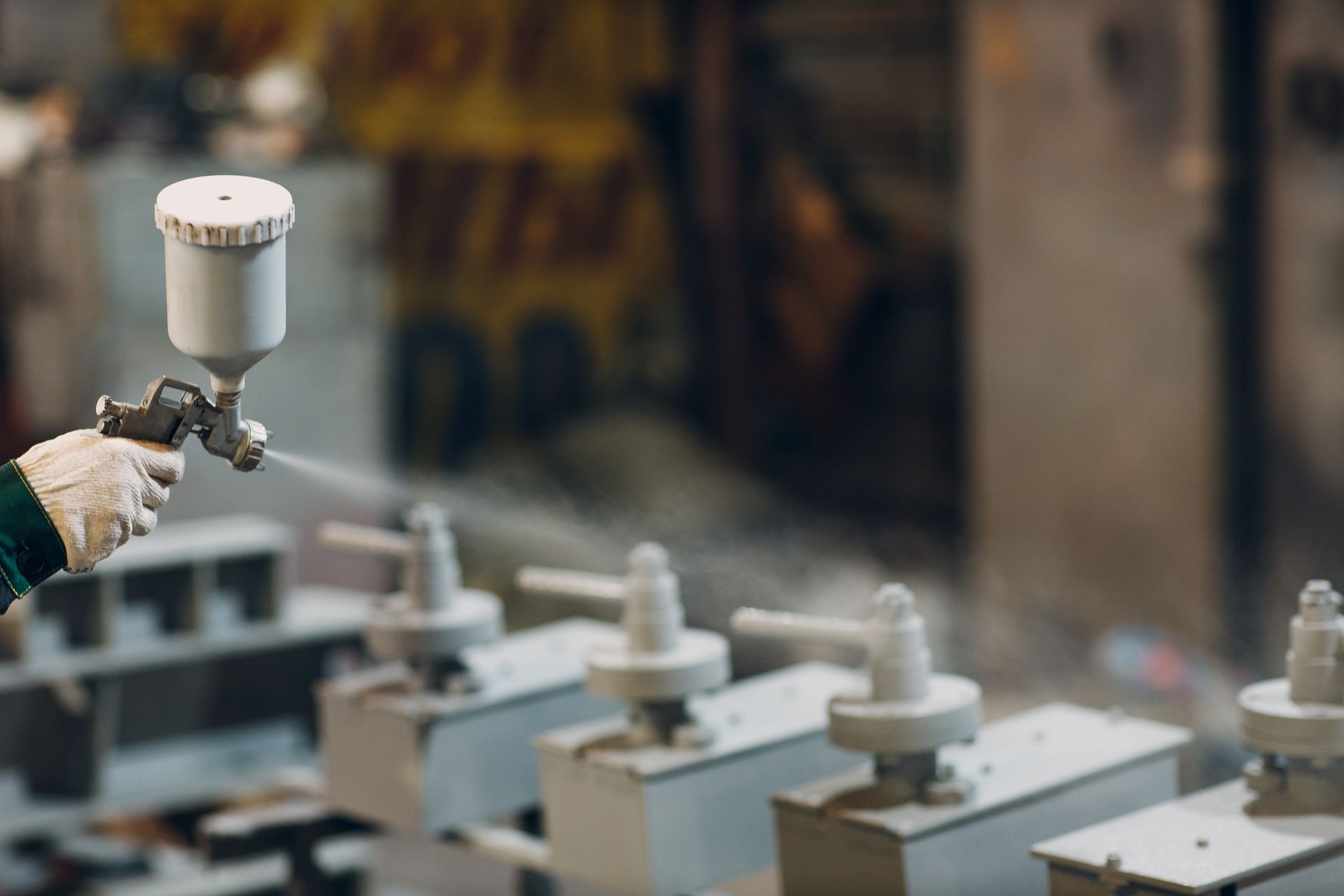 Person wearing a glove sprays coatings coatings on industrial equipment in a factory setting. 