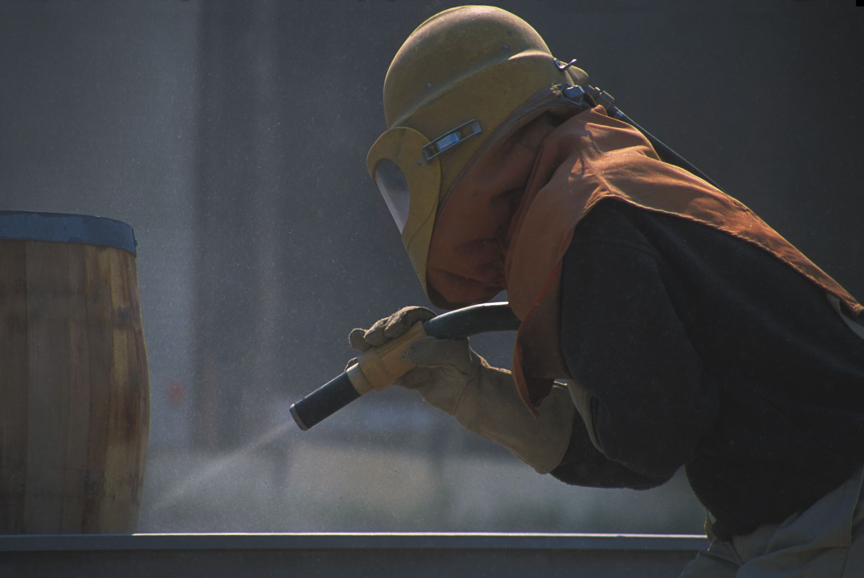 Person in protective gear sandblasting a wooden barrel.