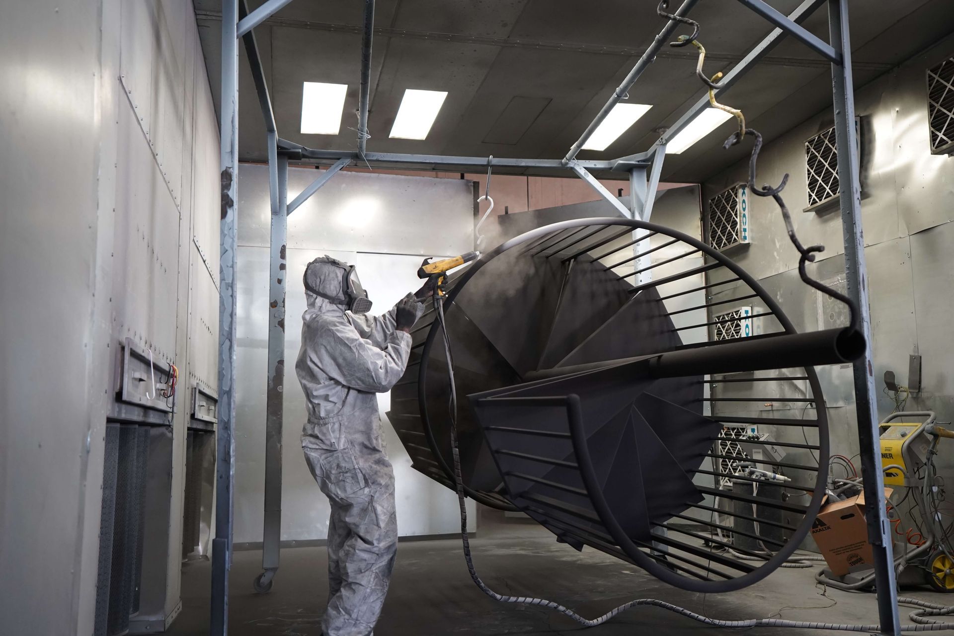 Technician in a white suit spray-paints a large aircraft part inside an industrial workshop.