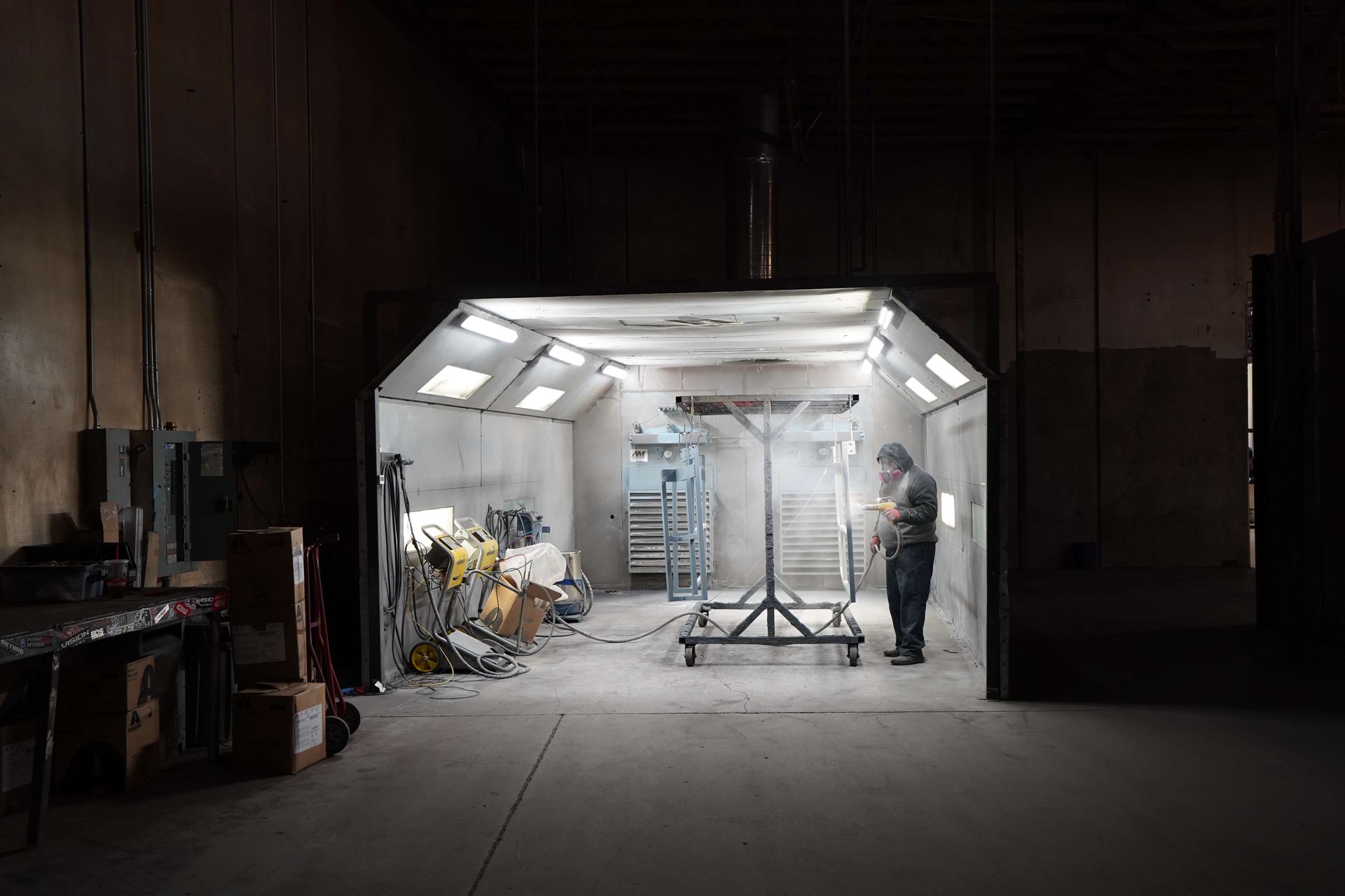 A man is standing in a paint booth coating some products with powder coat