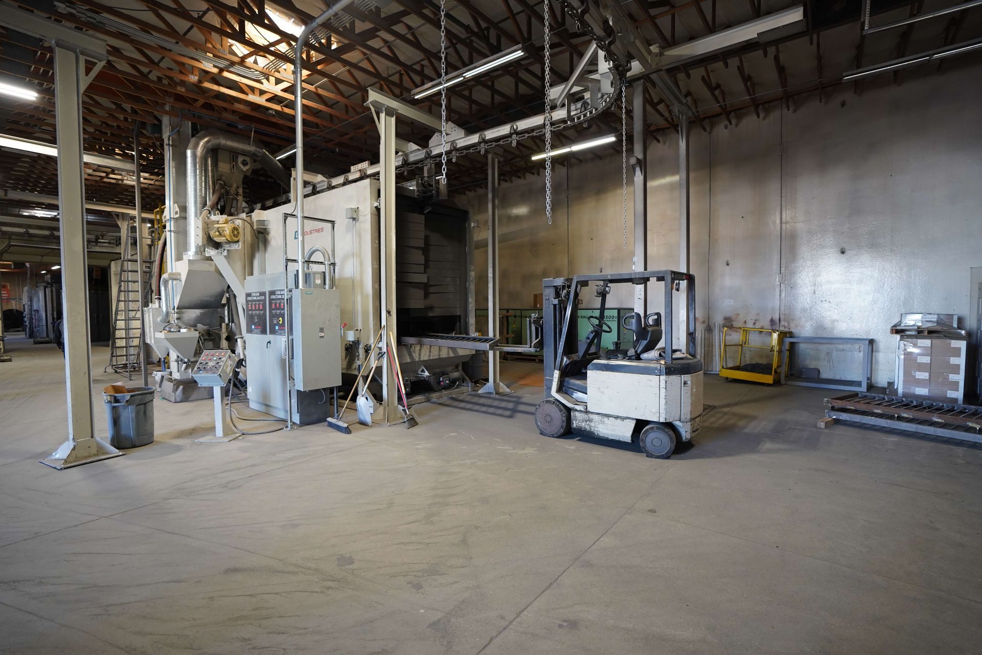 Forklift in a large industrial warehouse next to machinery and electrical controls.