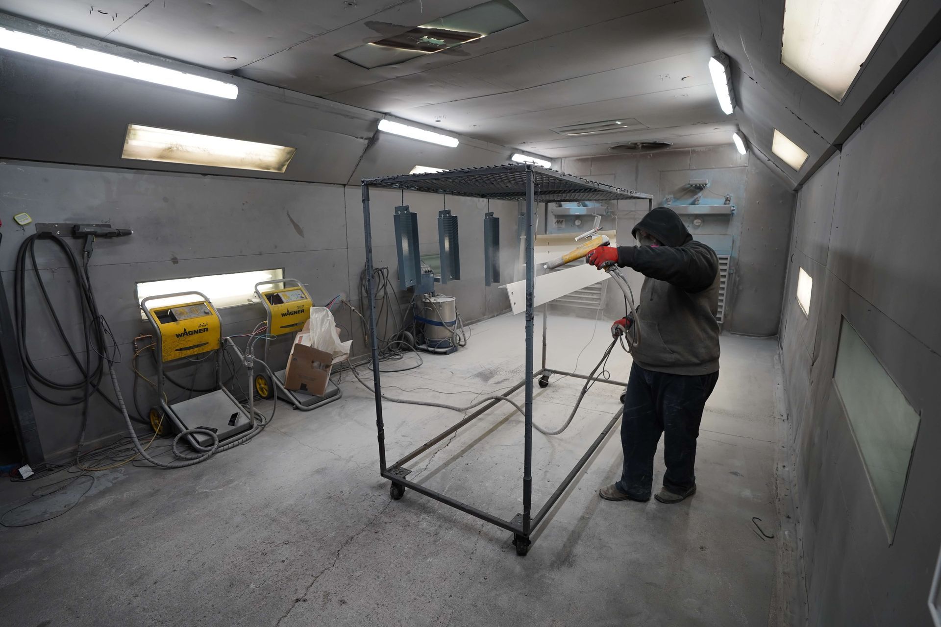 A man is painting a piece of metal in a paint booth. with powder coating tools