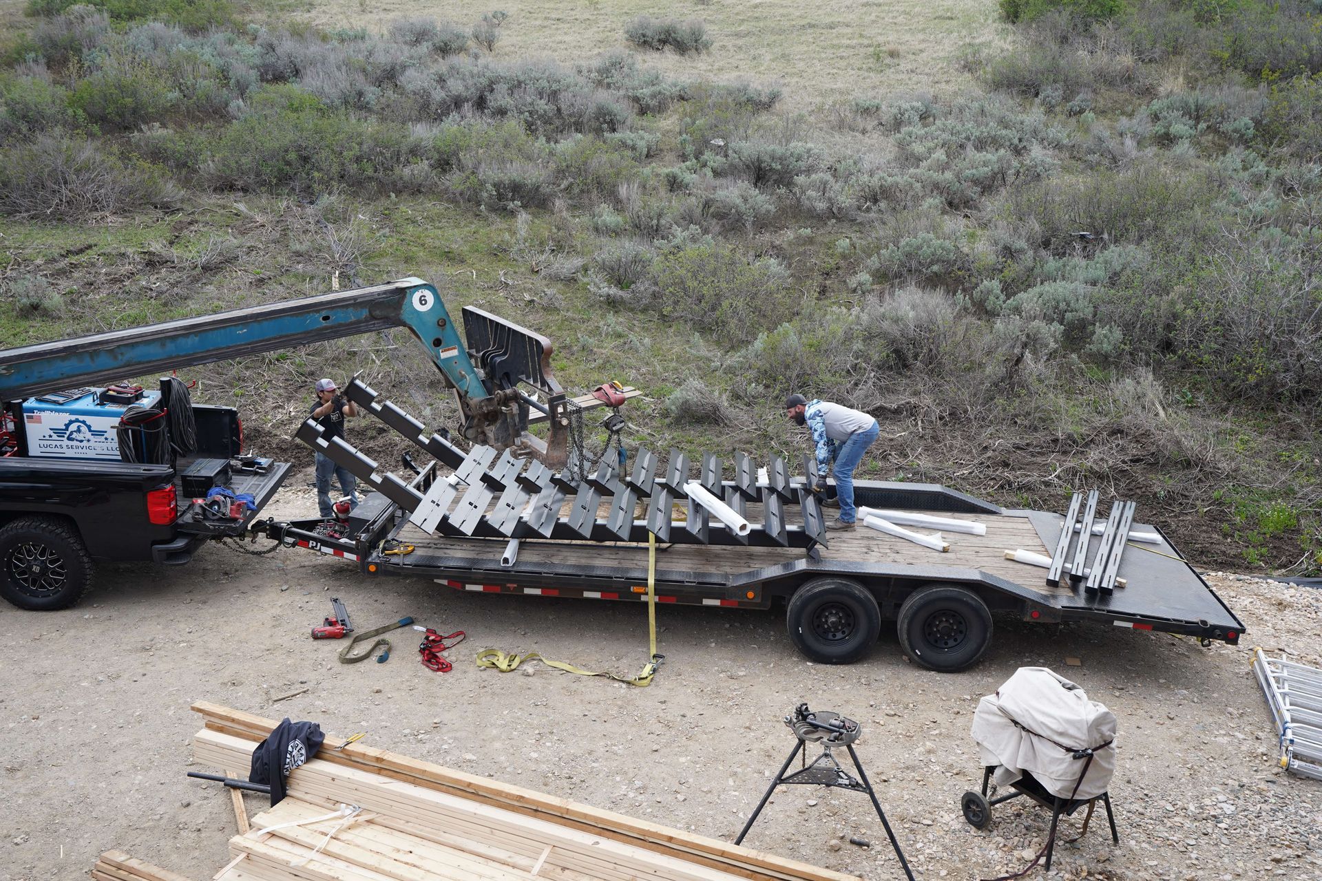 Tow truck loading a damaged trailer on a roadside, with a worker securing it and debris nearby.