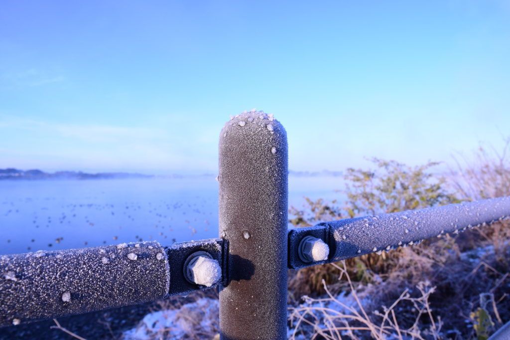 A close up of a frozen fence post with a lake in the background.