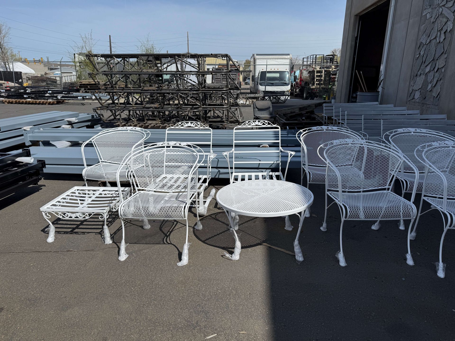 A bunch of white powder coated chairs and tables are sitting in a parking lot.