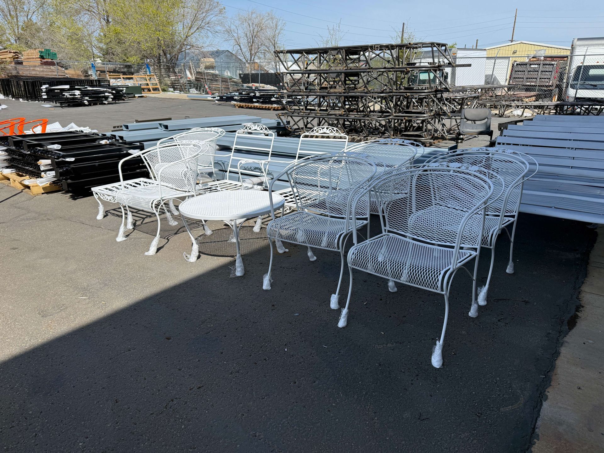 A bunch of white powder coated chairs and tables in a parking lot
