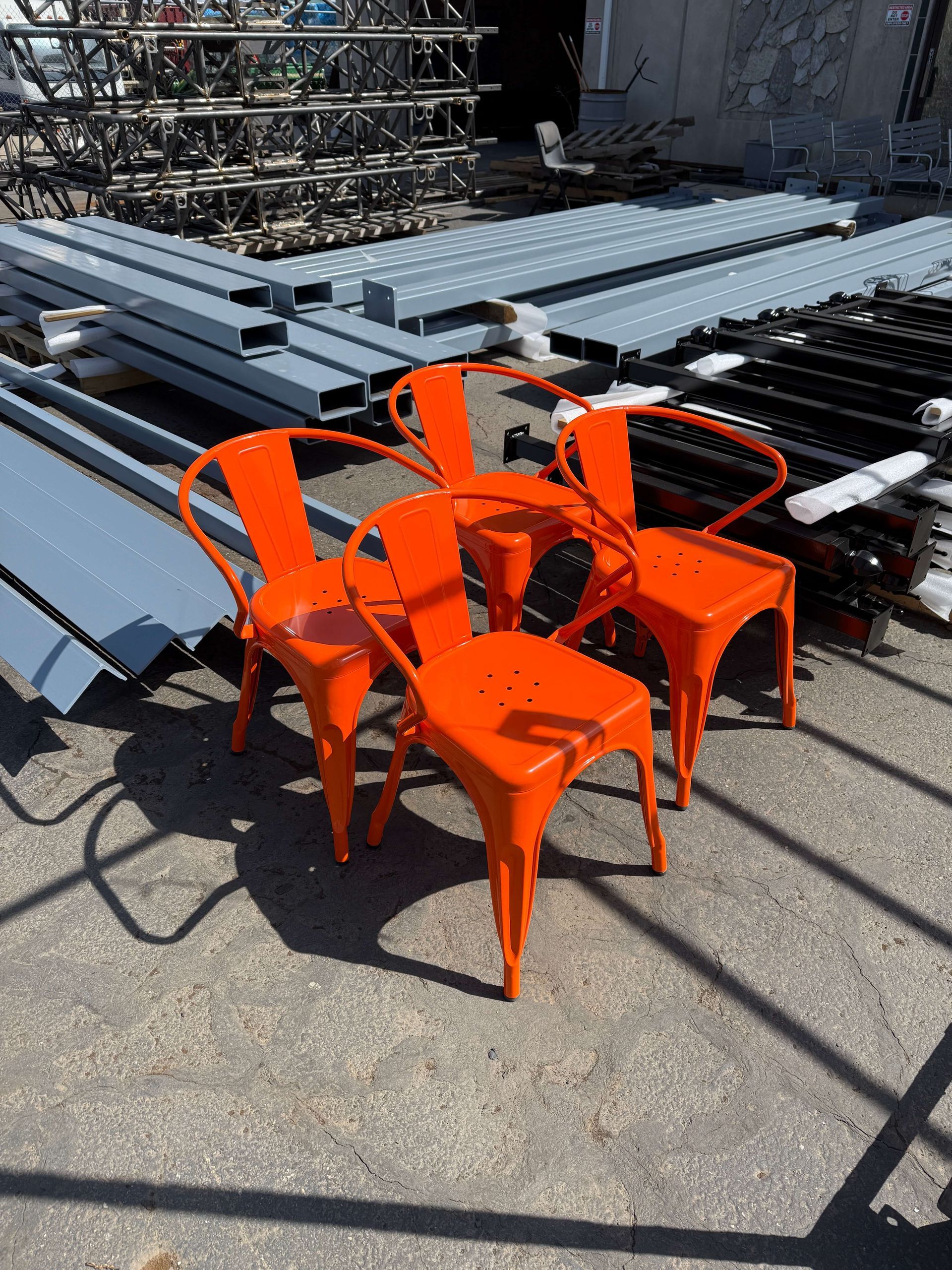 Four powder coated orange chairs are sitting in front of a pile of metal.