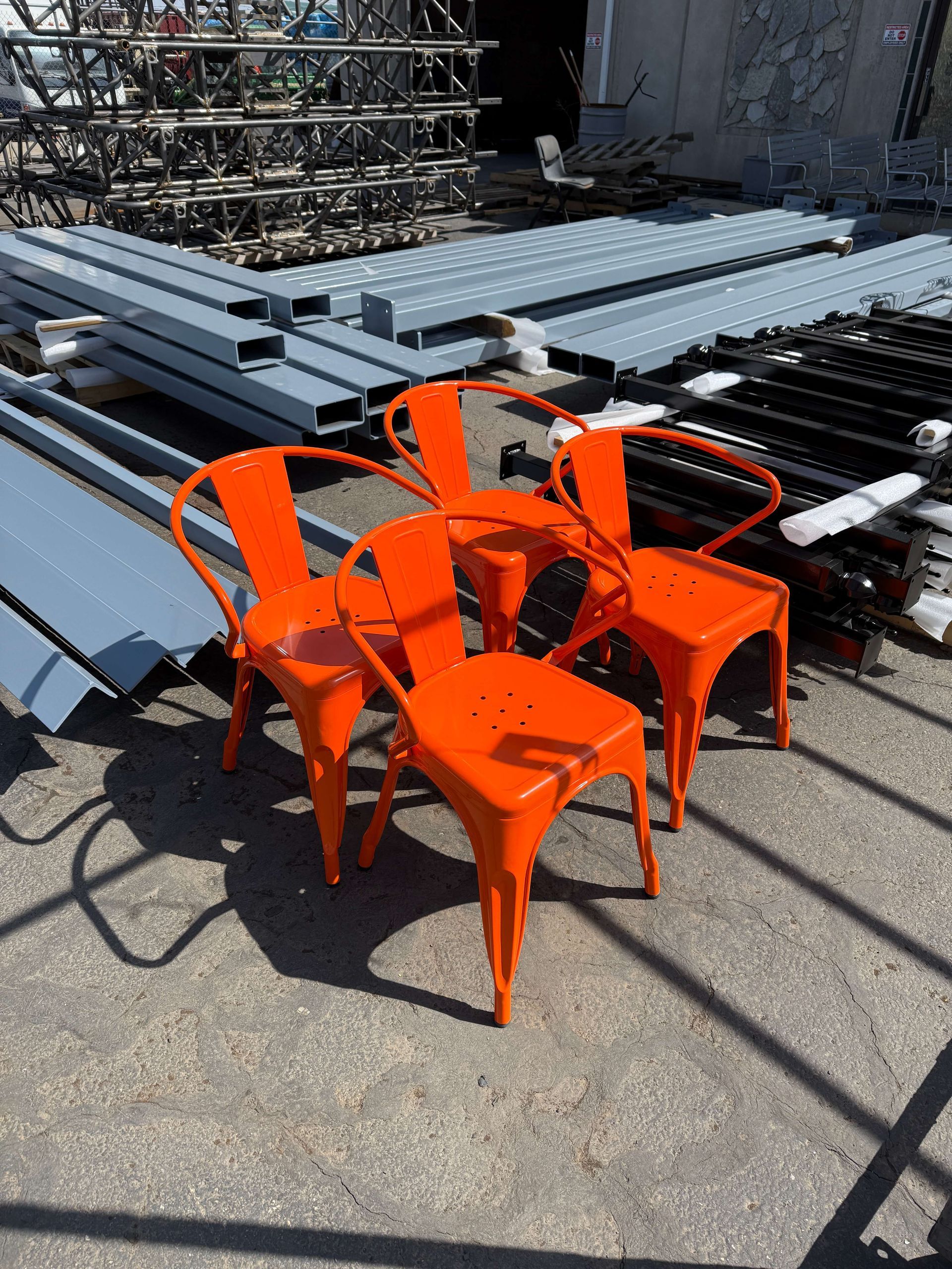 Four orange powder-coated chairs are sitting in front of a pile of pre-production metal waiting to get powder-coated.