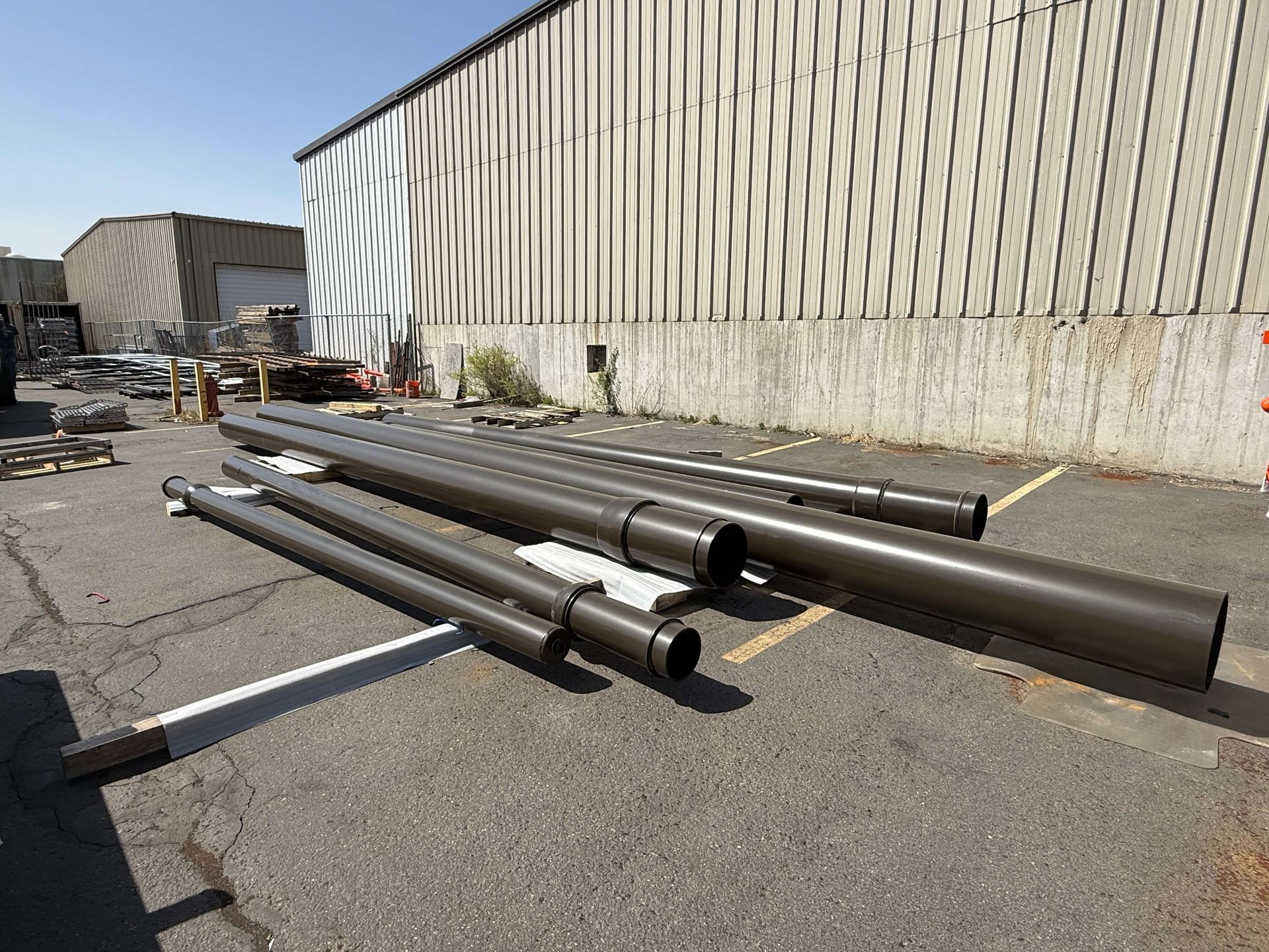 A bunch ofpowder coated pipes are stacked on top of each other in a parking lot in front of a building.