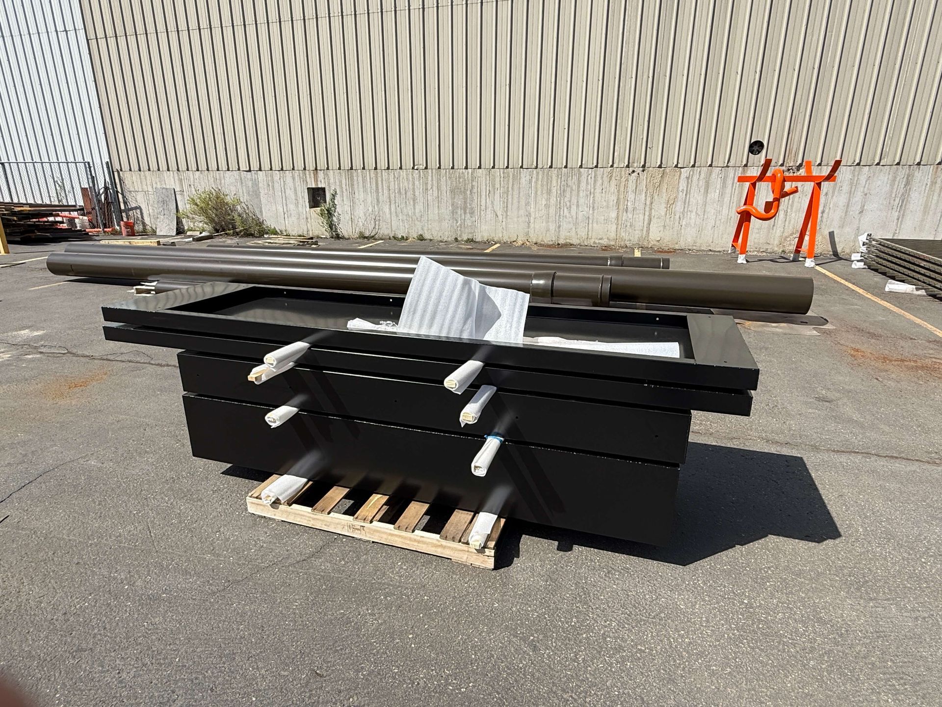 A stack of black powder coated boxes sitting on top of a wooden pallet in a parking lot.