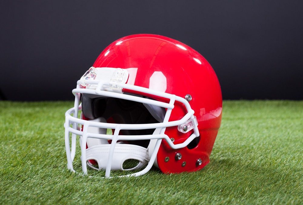 A red football helmet is sitting on top of a green field.