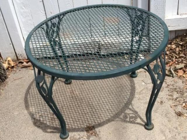 A green metal table is sitting on a sidewalk in front of a white fence