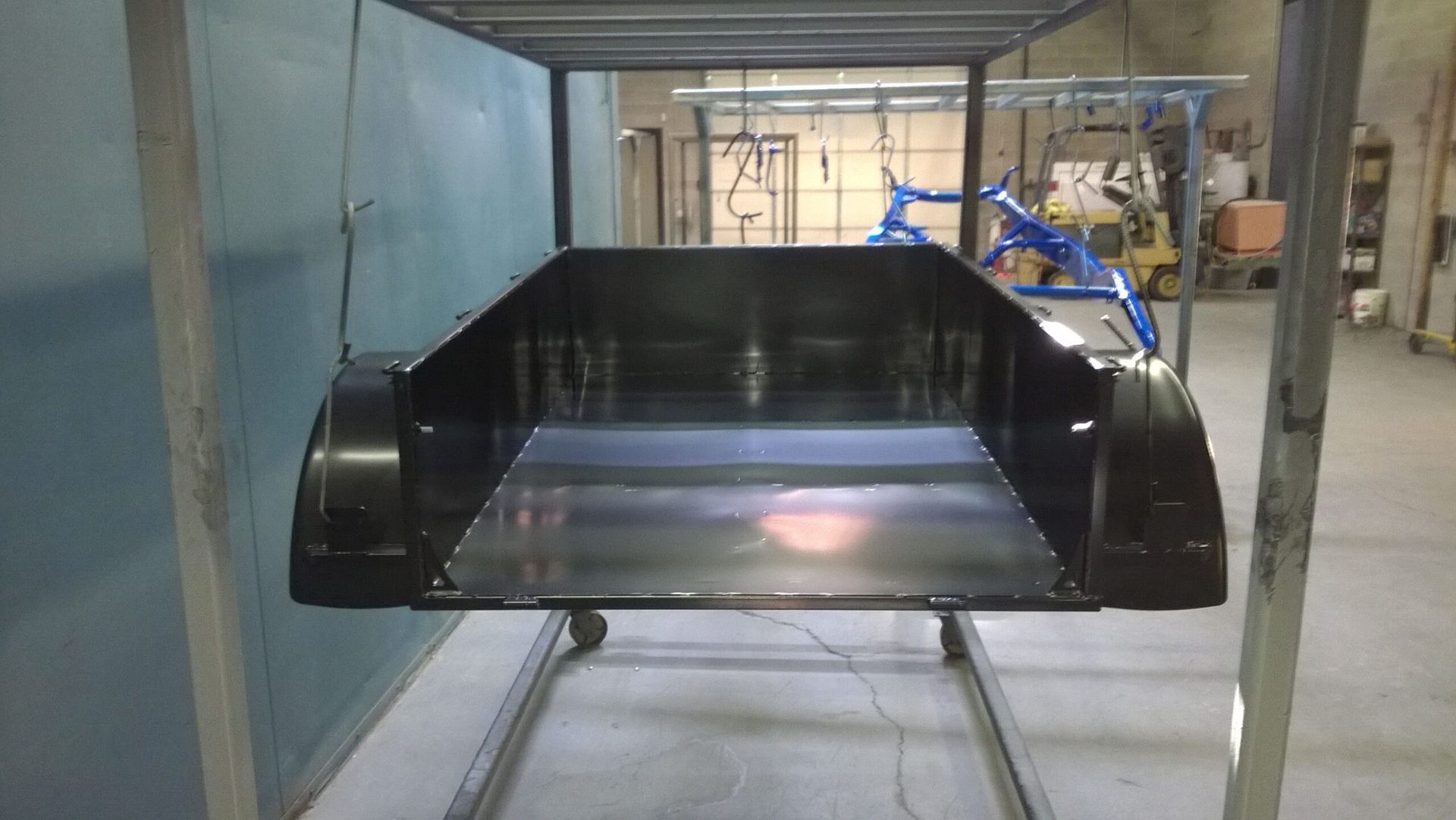 A black trailer is being painted in a factory