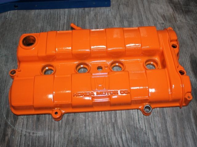 A close up of an orange valve cover on a wooden table.