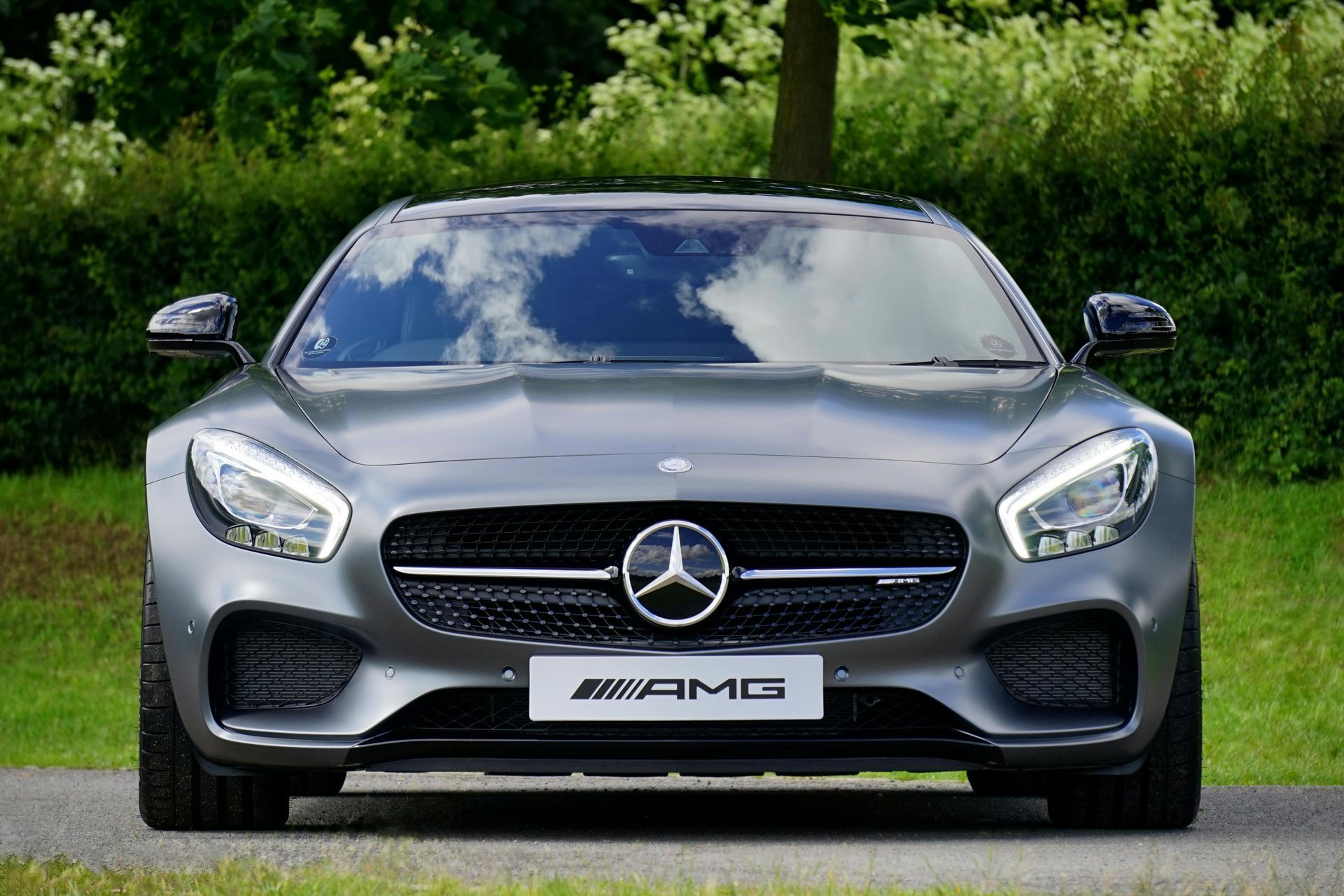Gray Mercedes-AMG sports car parked on grass, front view, with trees in the background.