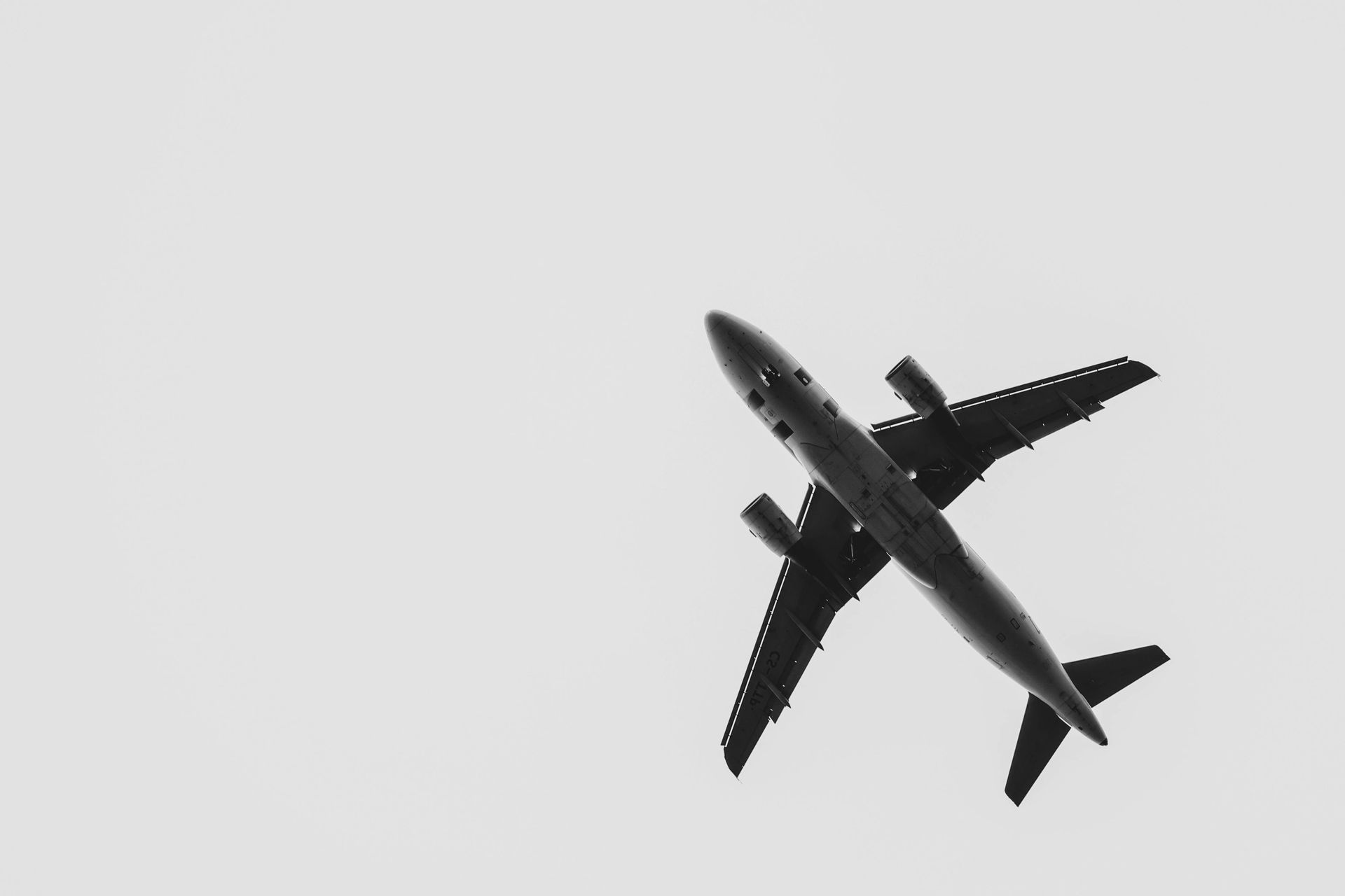 Airplane, viewed from below, ascends in a gray sky.