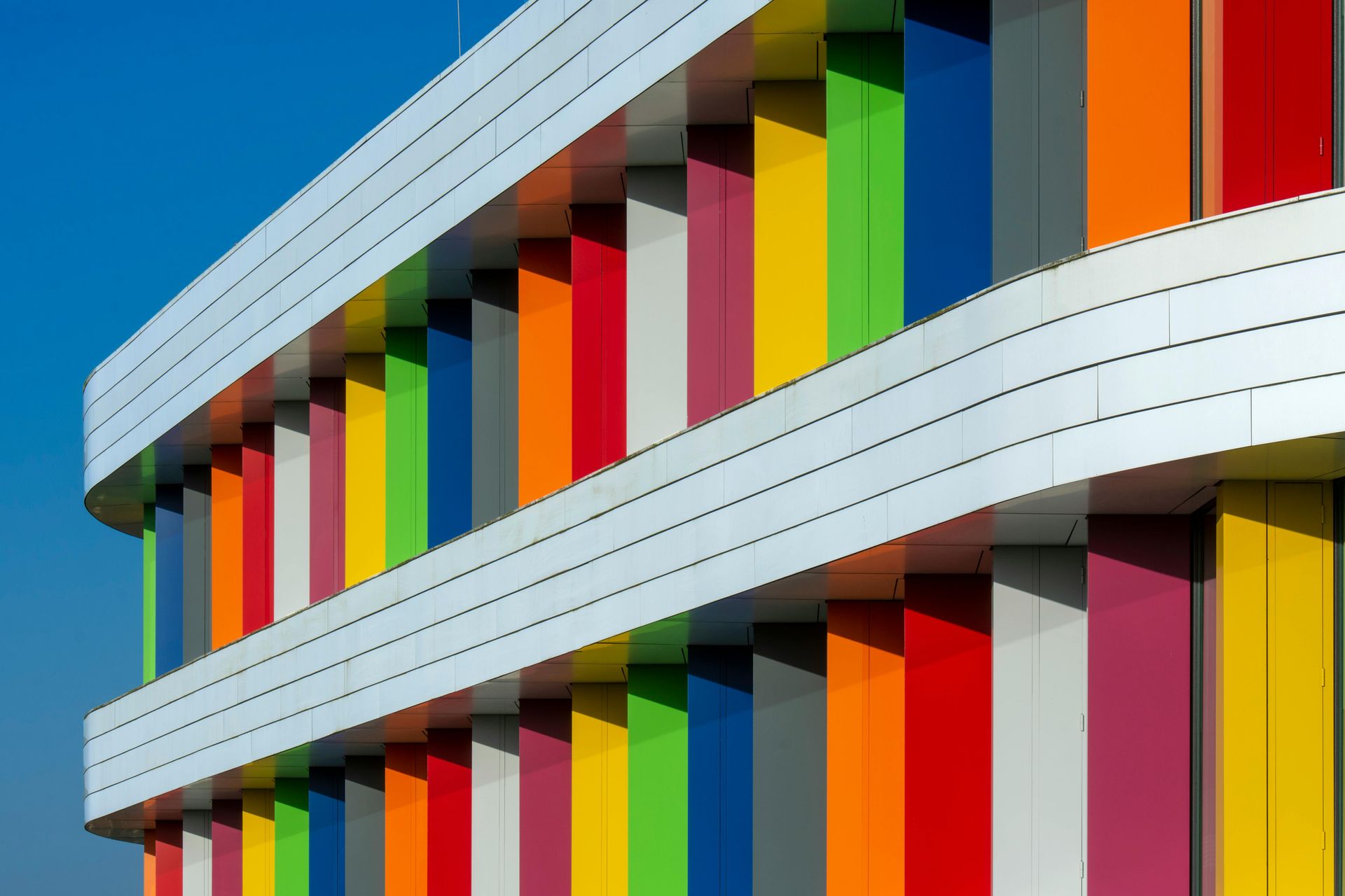 Modern building facade with bright multicolored vertical panels and white curved bands