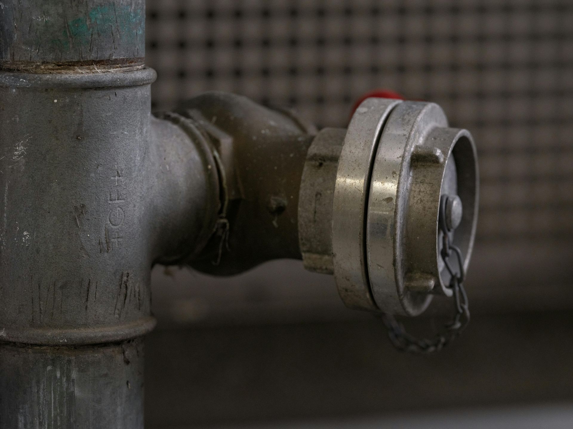 Fire hose connection on a metal pipe; silver with red cap, against a blurred background.