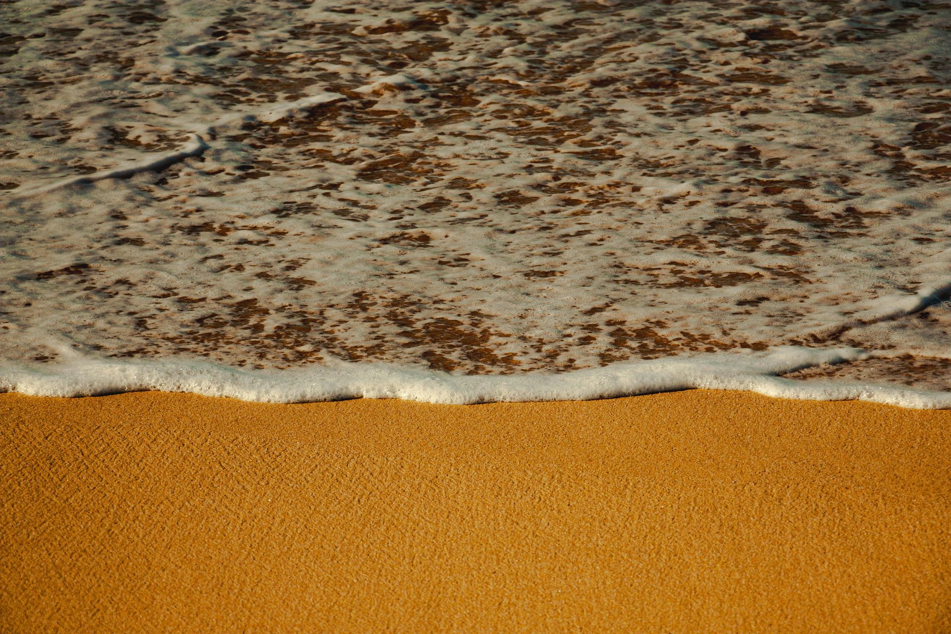 Sandy sable beach with foamy ocean waves gently washing ashore.