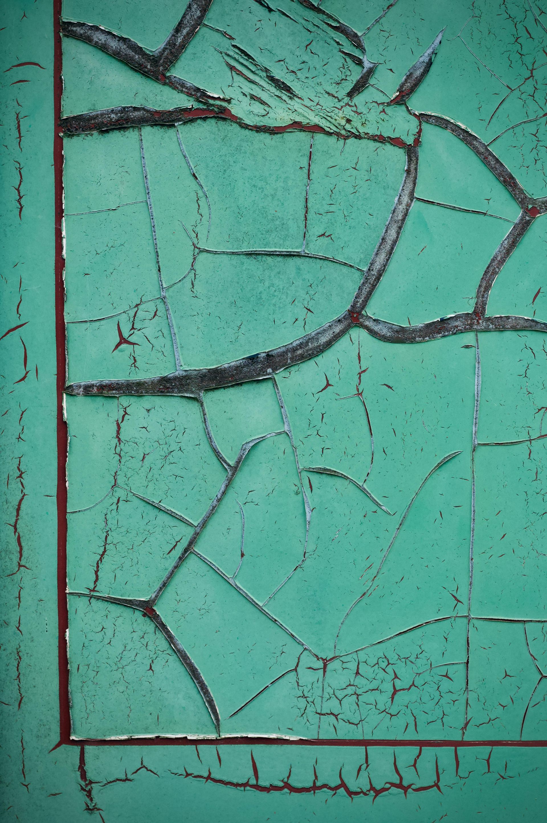 Close-up of cracked turquoise painted surface with dark fissures and a thin border line