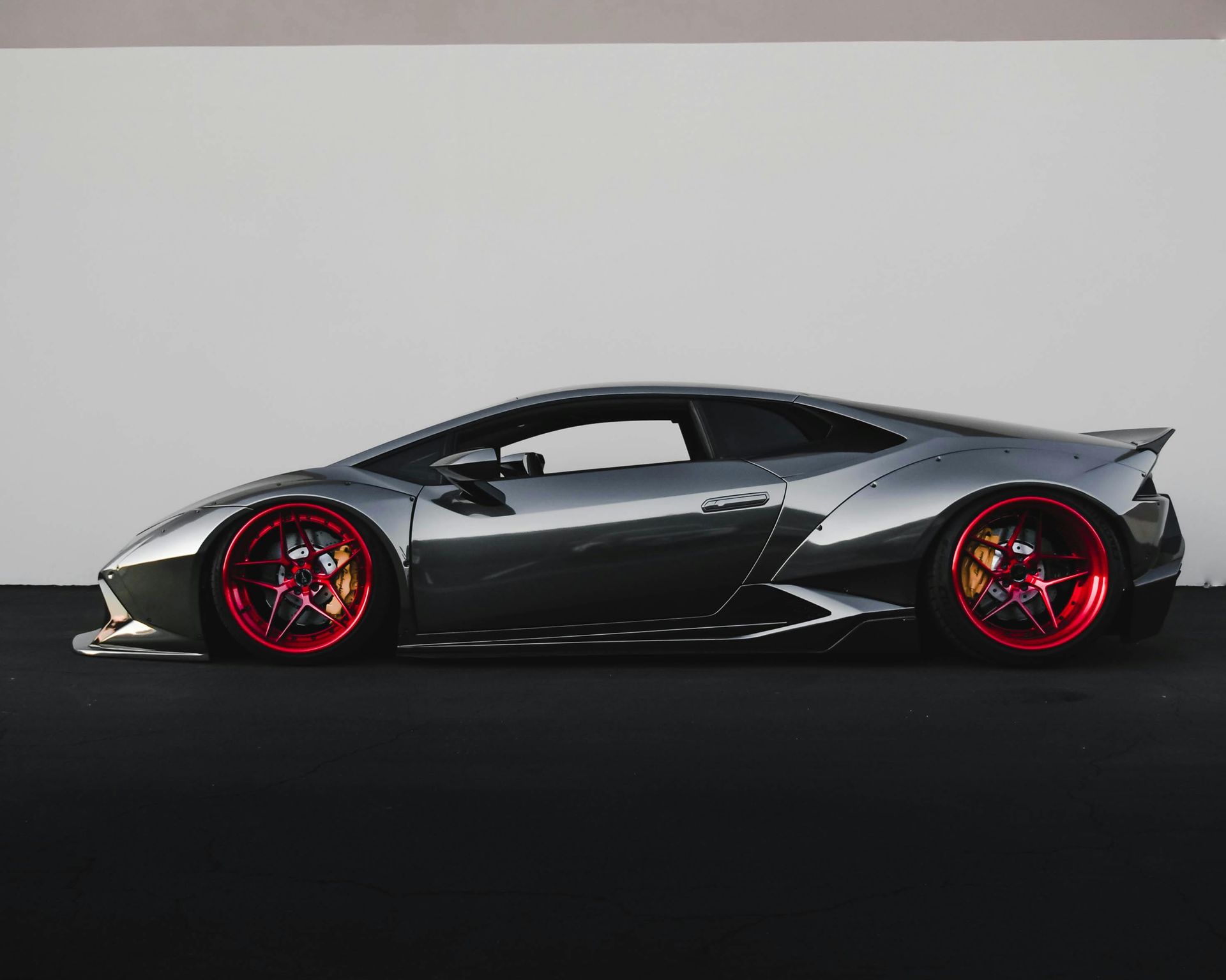 Gray sports car with red powder coated rims parked on black surface against a white wall.