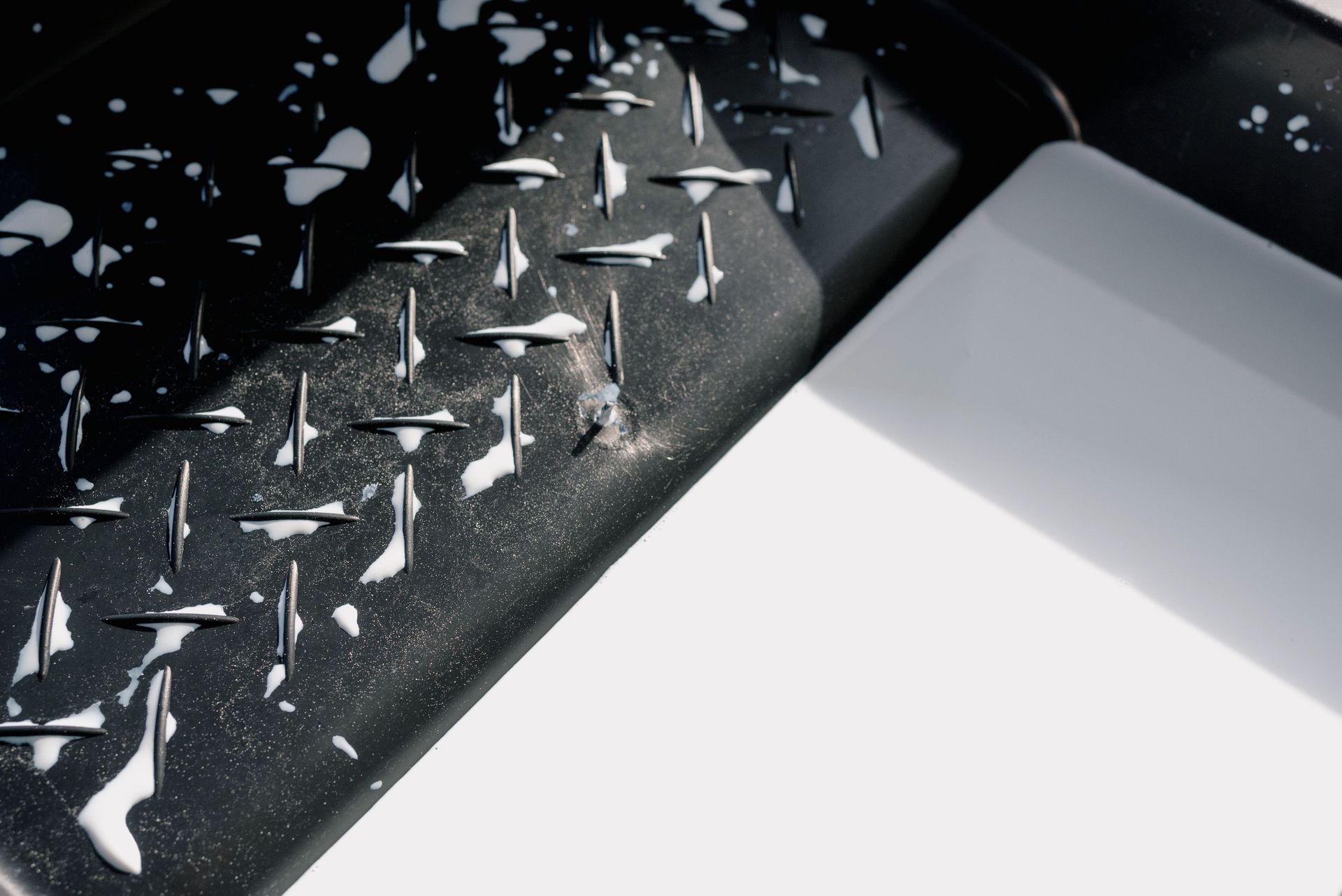 Close-up of a black surface with scattered white paint chips beside a white sheet of paper