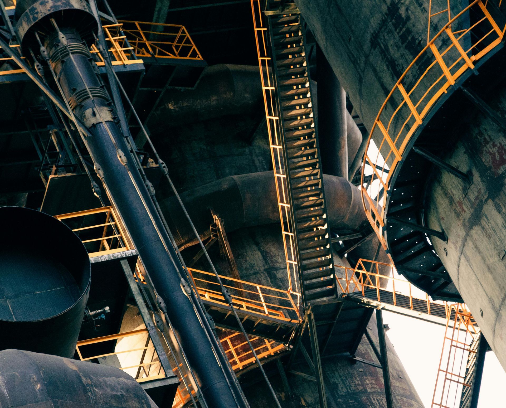 Industrial interior with towering metal stairs, pipes, and catwalks in a dimly lit factory