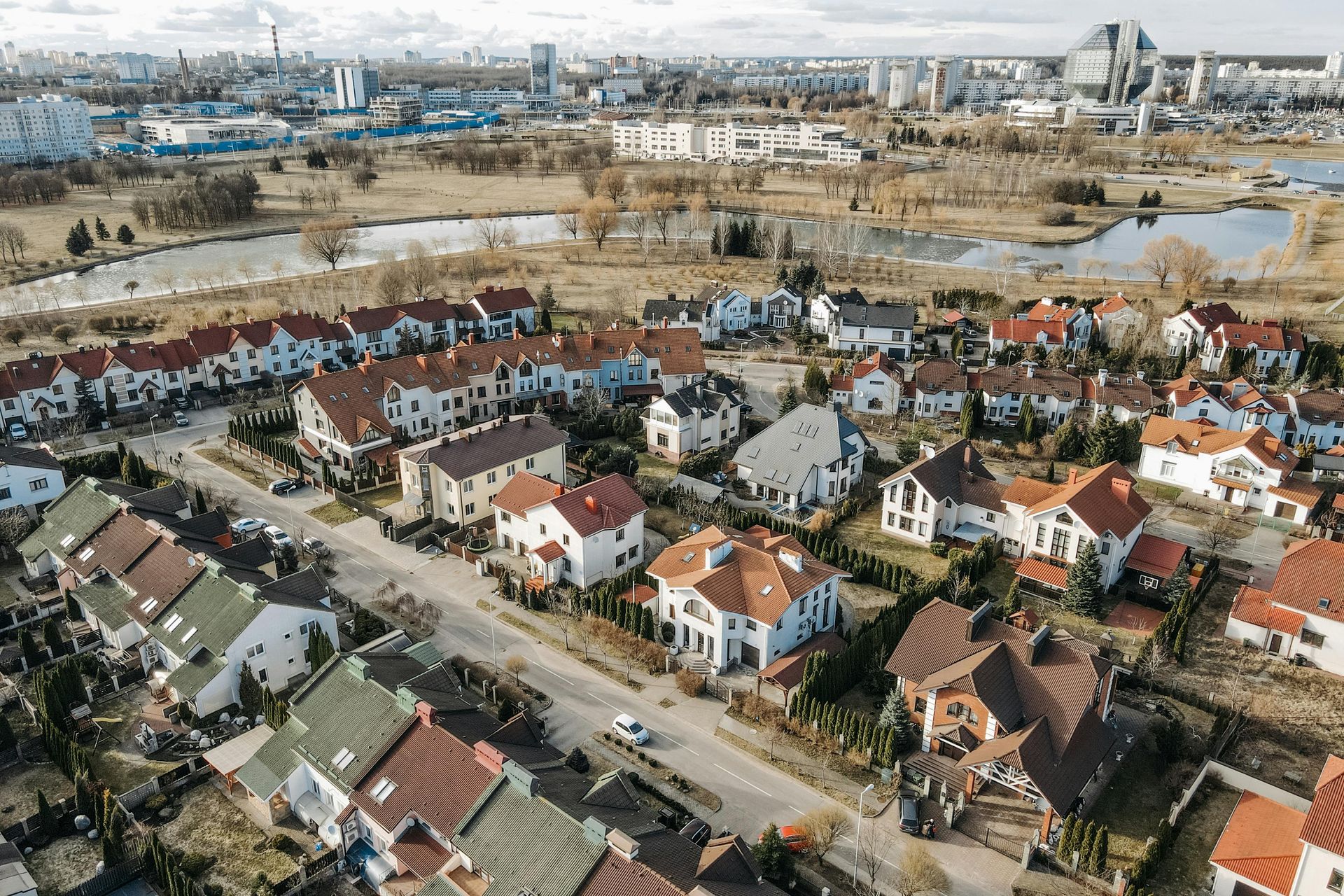 Aerial view of a suburban neighborhood with rows of houses, trees, and a city in the background.
