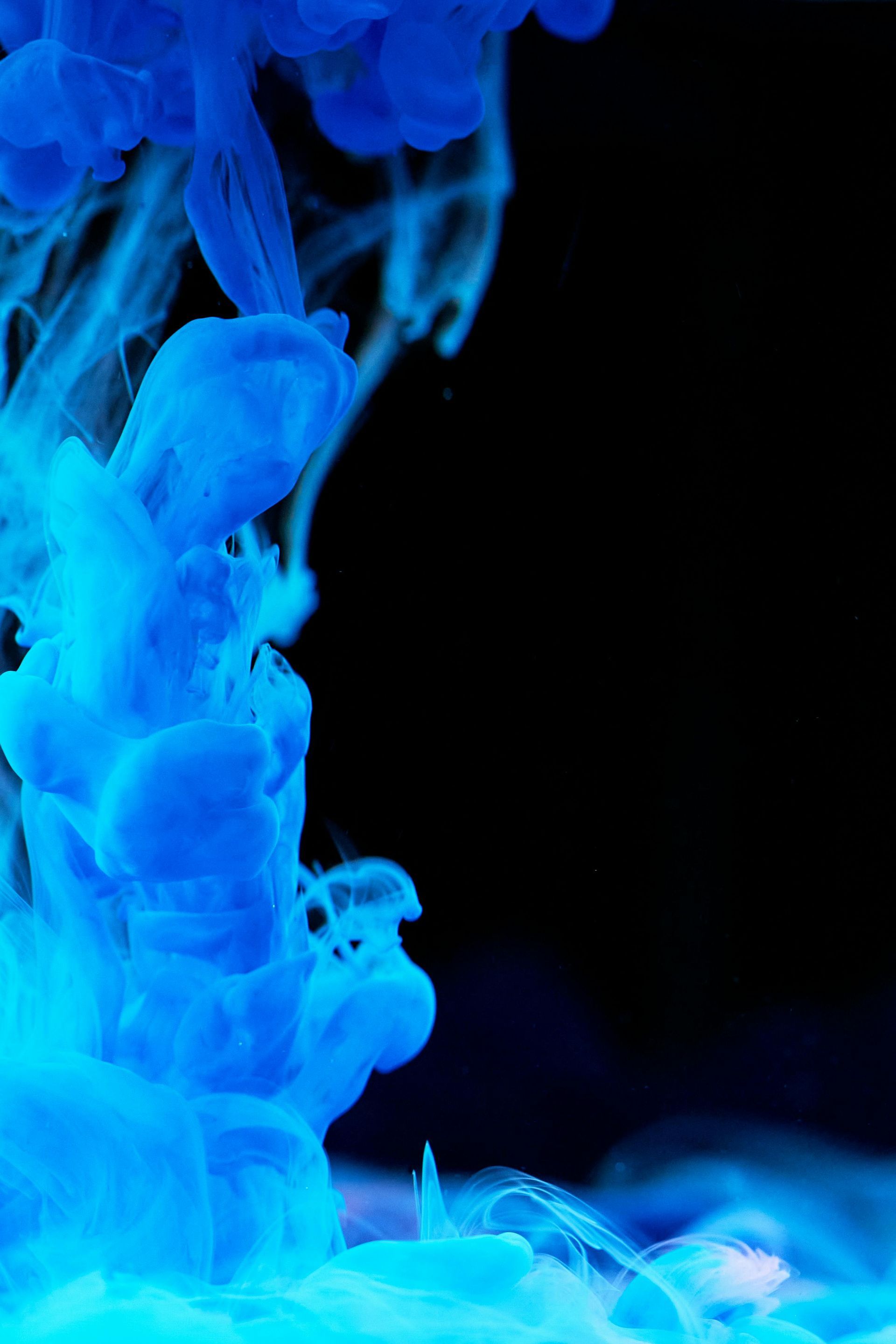 Vibrant blue ink swirls through water against a dark black background.